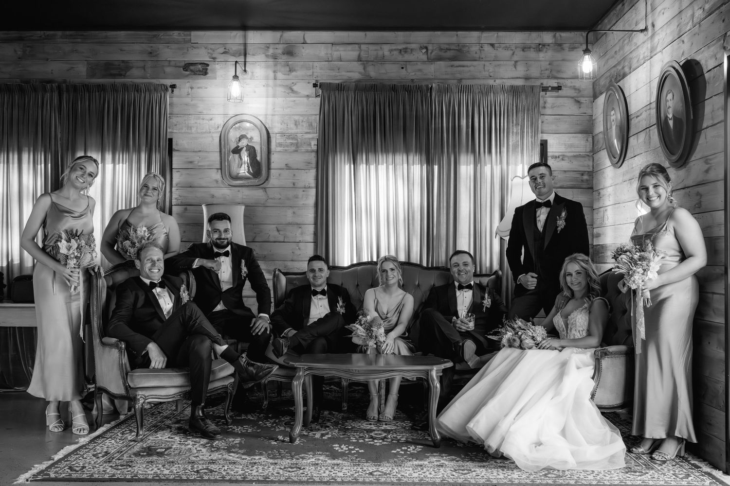 A vintage black and white wedding party photograph shows a group gathered in an elegant wood-paneled room.