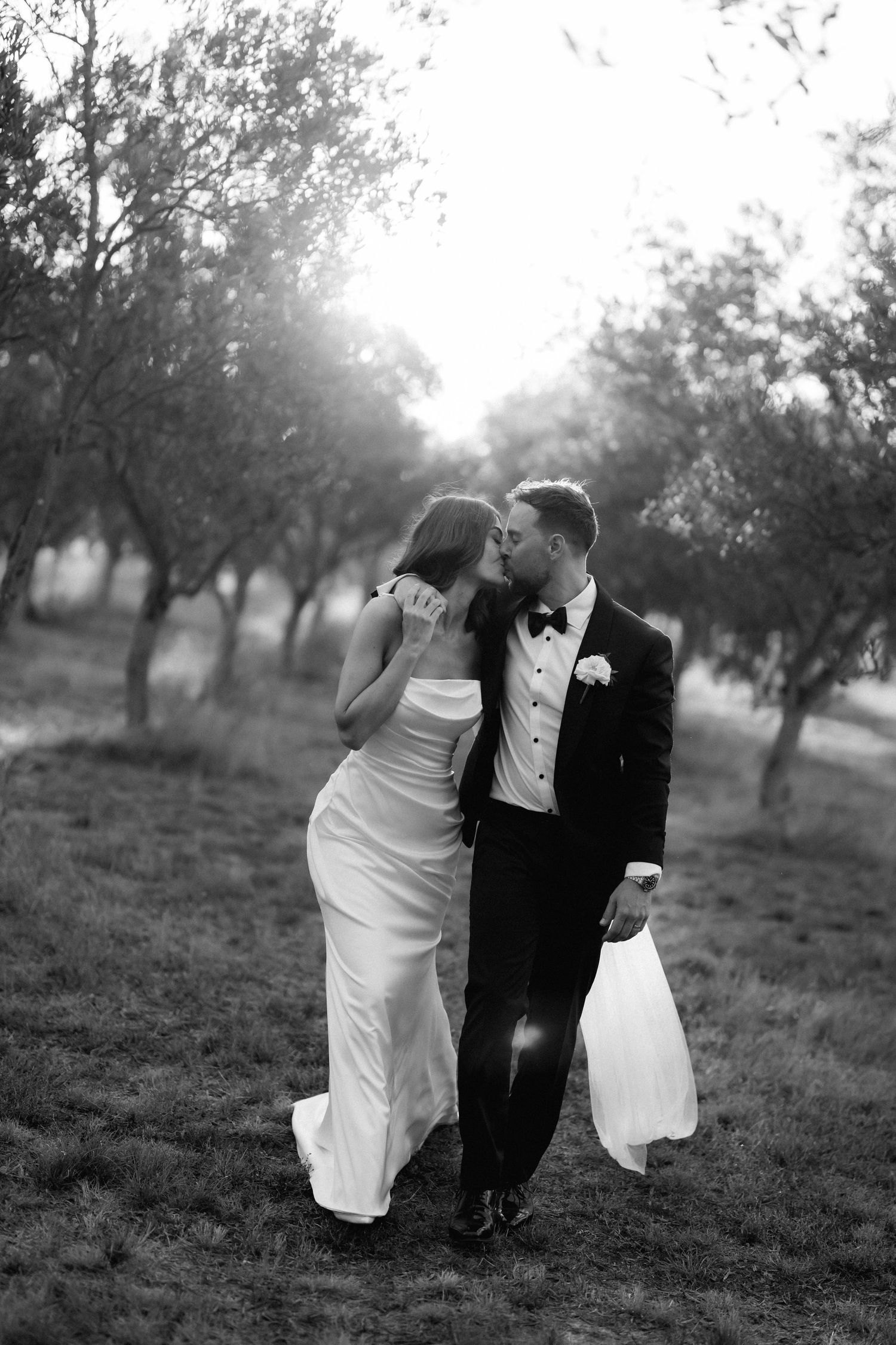 Black and white romantic portrait of newlyweds in an orchard during sunset.