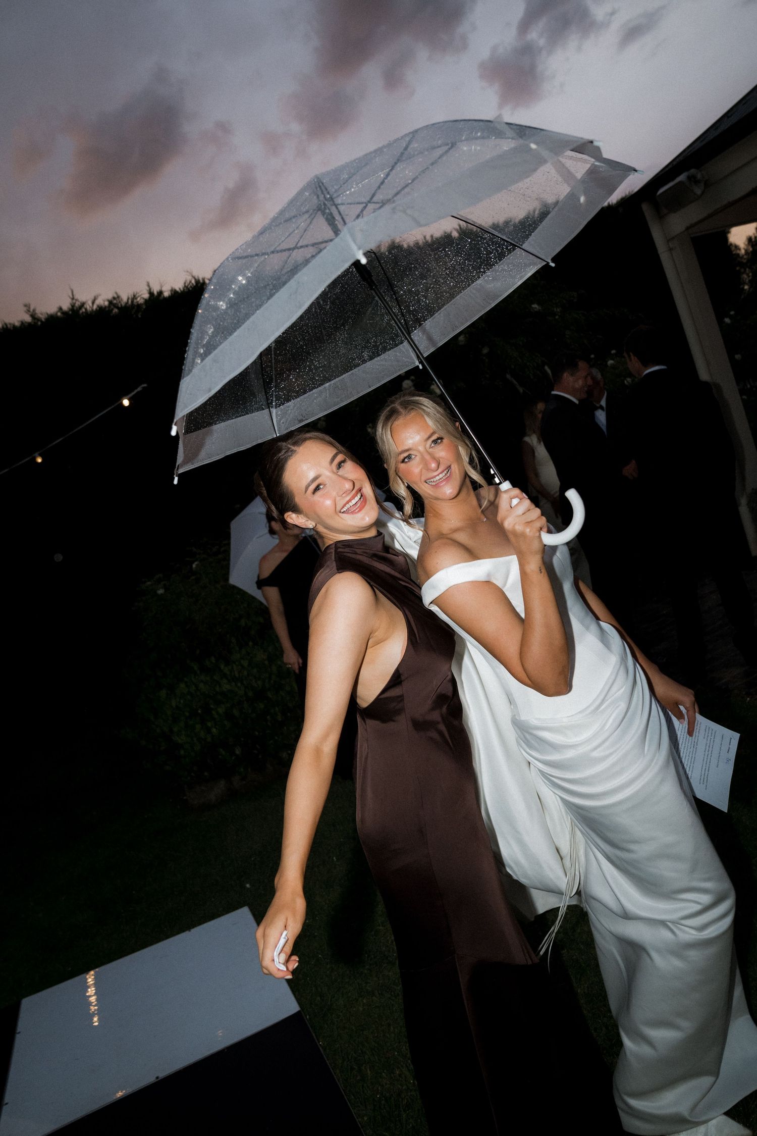 Wedding guests sharing laughs under clear umbrellas during evening celebration.