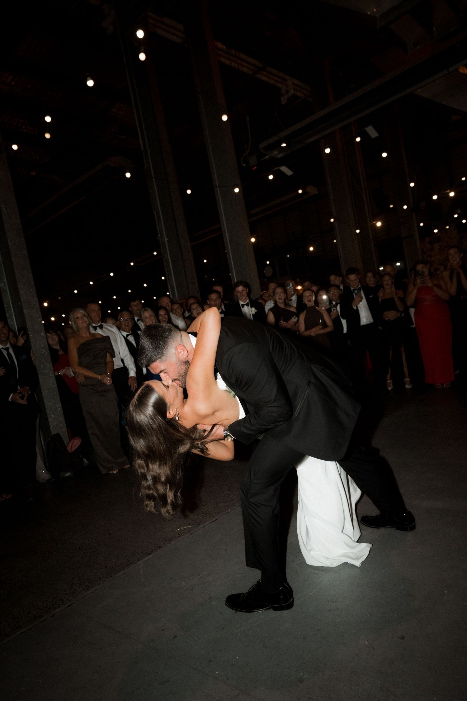 Newlyweds execute a romantic dance dip move on their wedding day under twinkling lights.