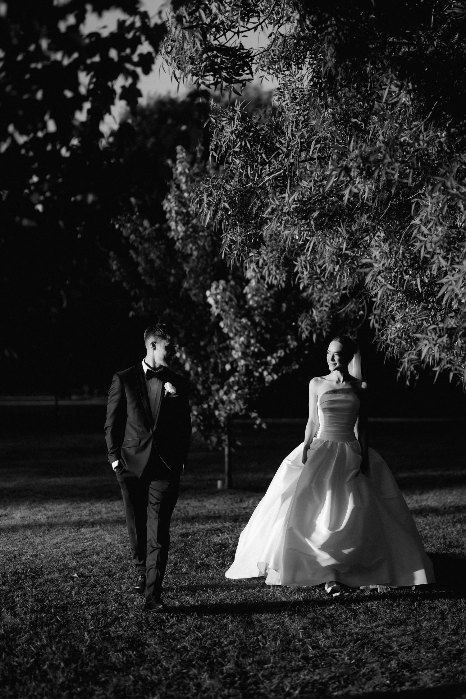 A dramatic black and white wedding portrait captured under evening trees.