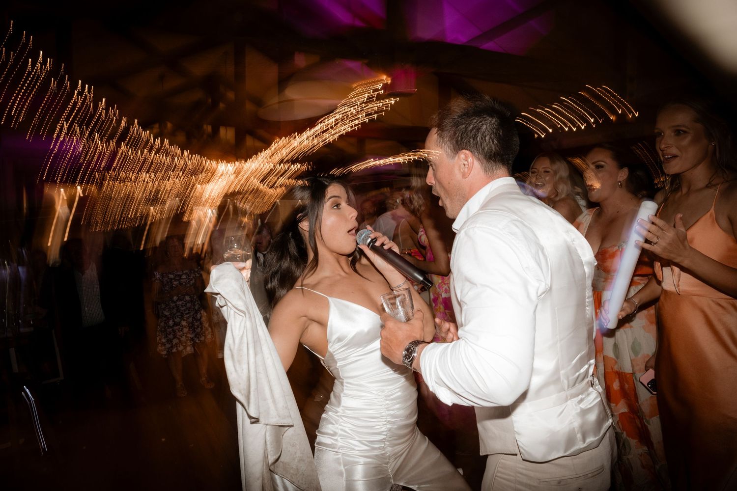 Wedding reception dance floor filled with celebrating guests under purple lighting.