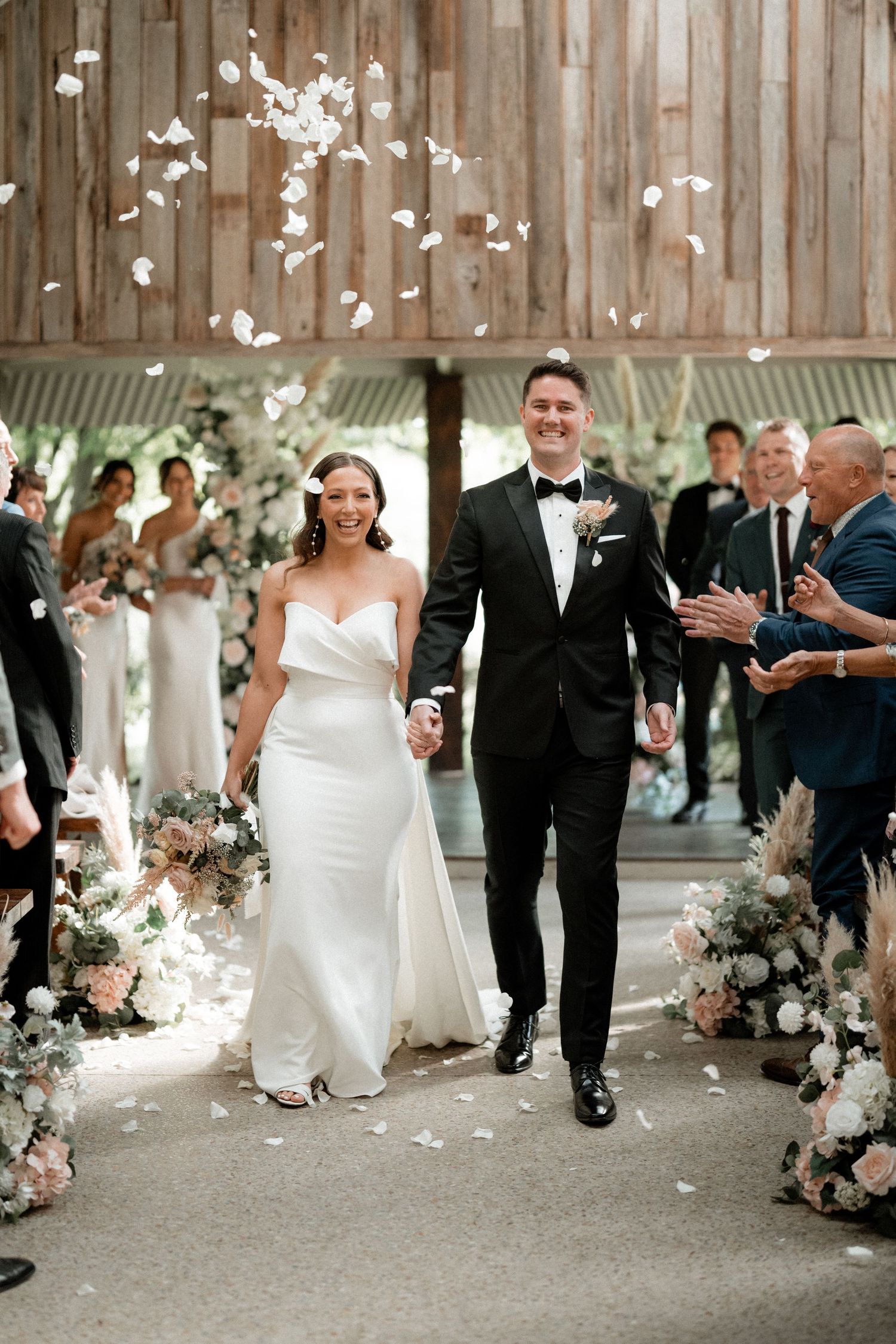 Joyful wedding ceremony exit with flower petals and floral decor lining the aisle.