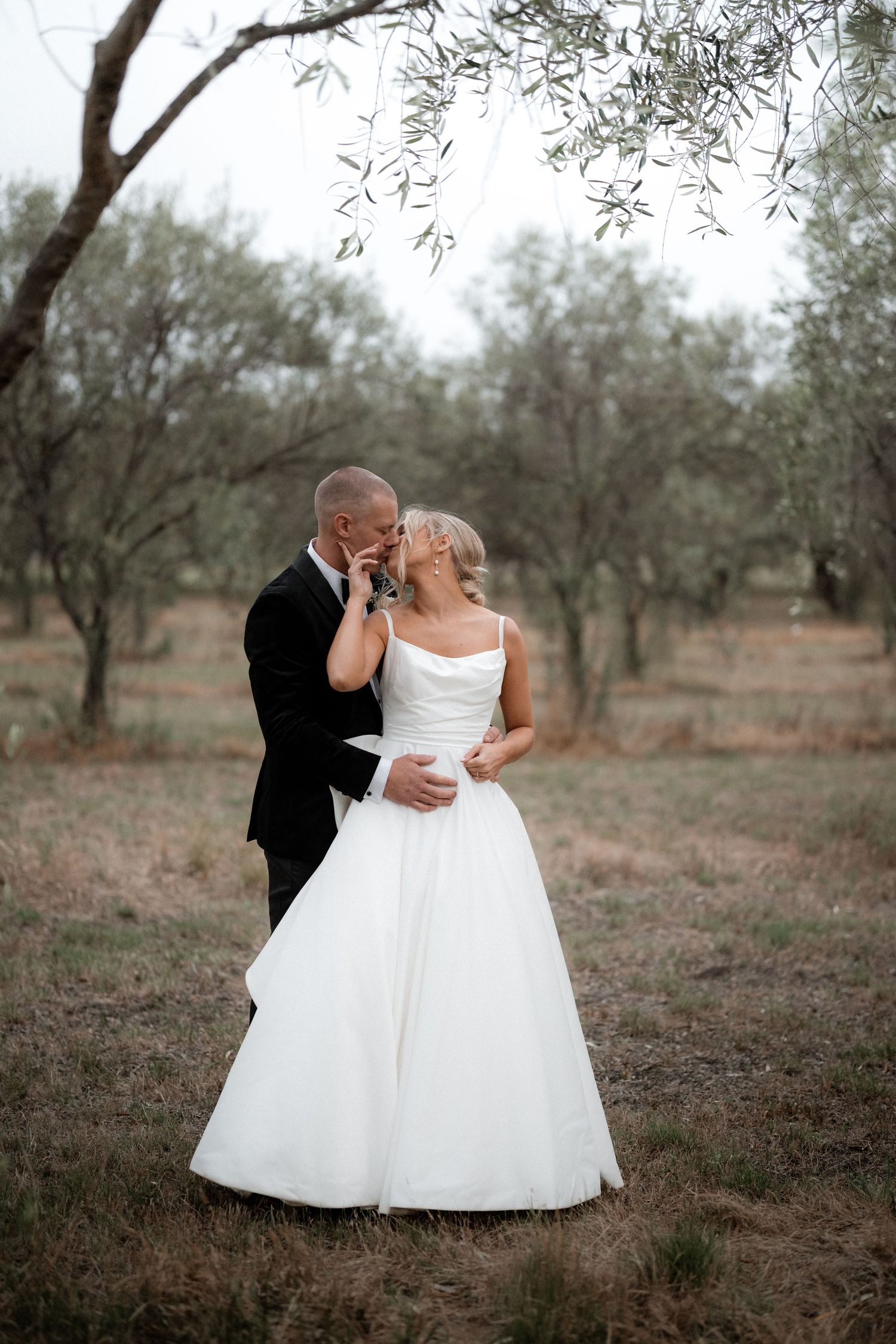 Romantic wedding moment captured in olive grove with classic black and white attire.