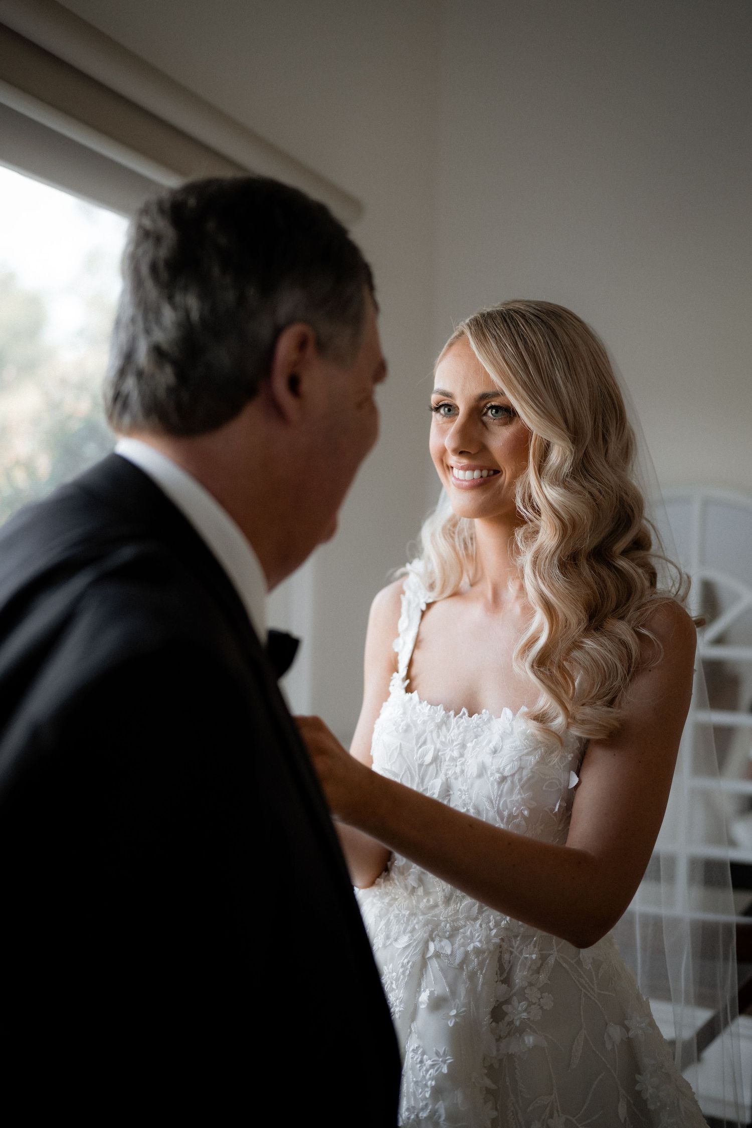 An emotional moment between a bride in white lace gown and someone in formal attire.