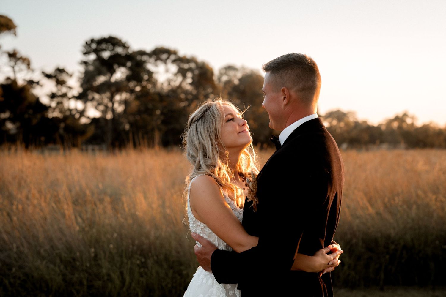 A couple shares an intimate moment in a sun-lit field during golden hour at their wedding.