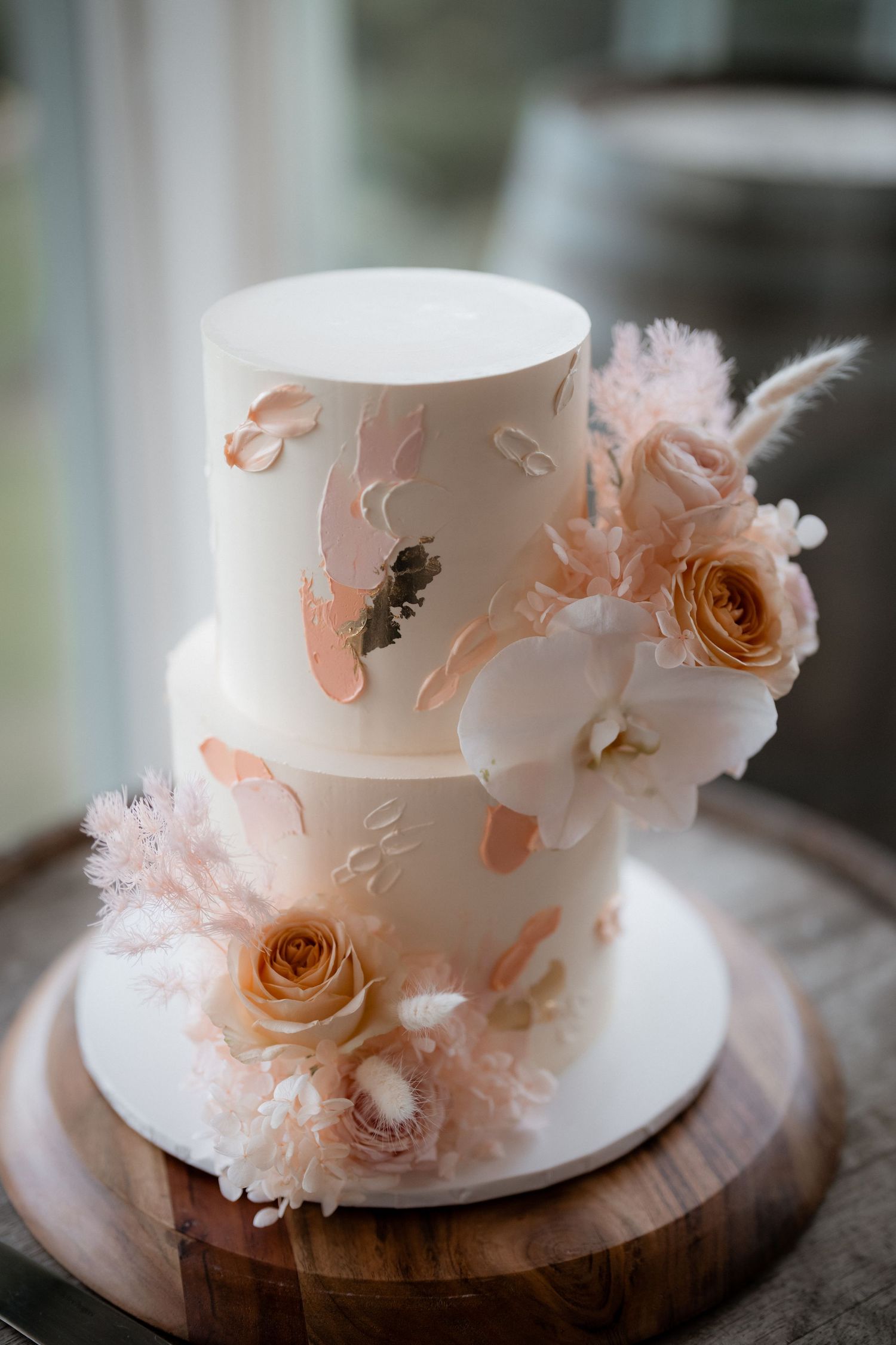 Two-tier white wedding cake decorated with blush roses and butterfly details on wooden stand.