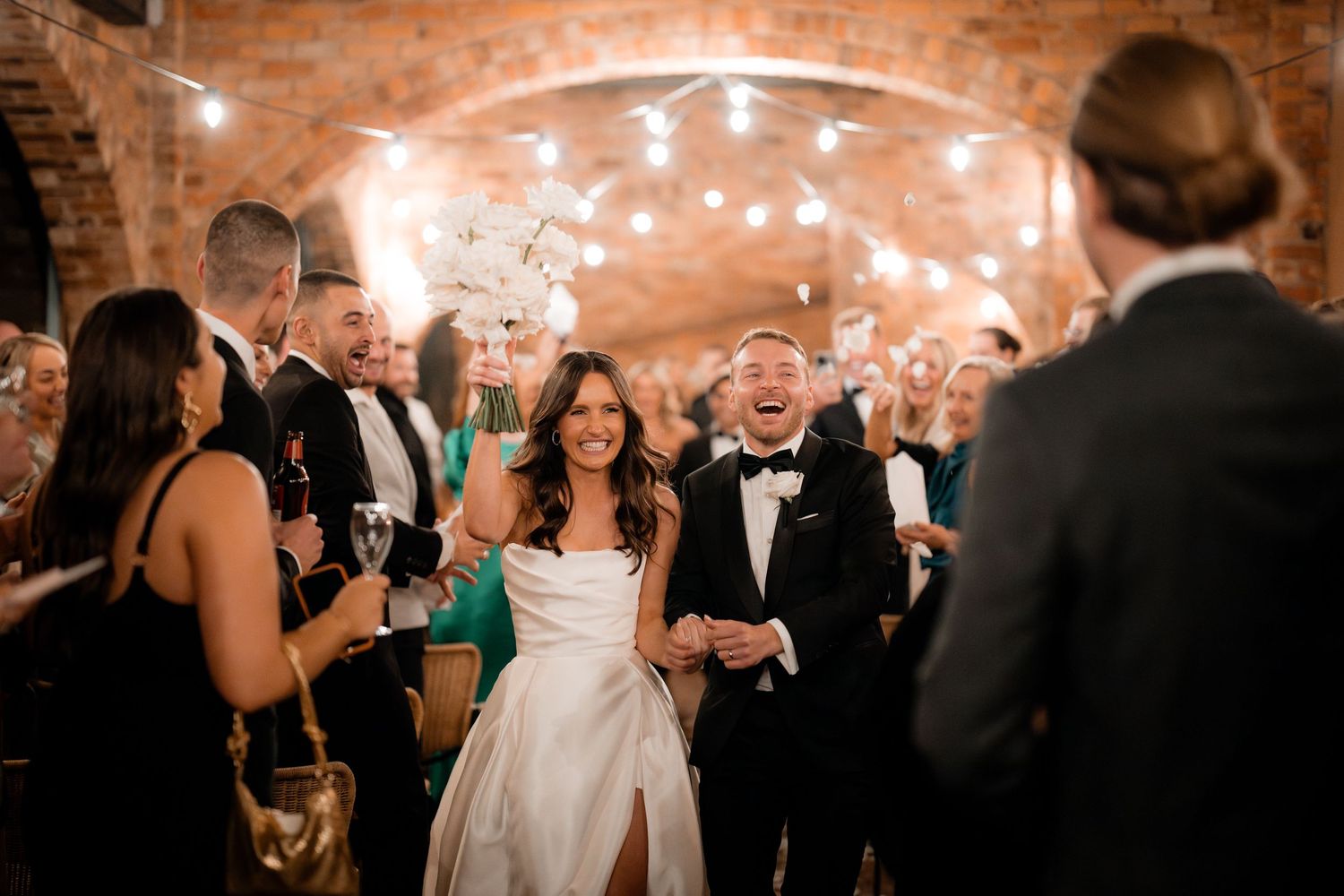 Wedding celebration in rustic brick venue with string lights overhead.