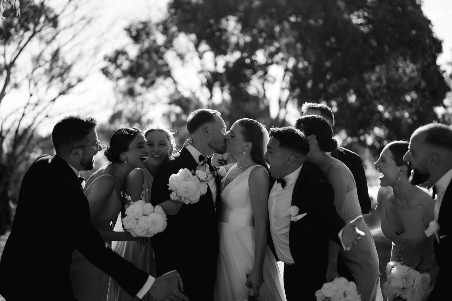 Wedding guests gathered outdoors for ceremony with floral arrangements visible.