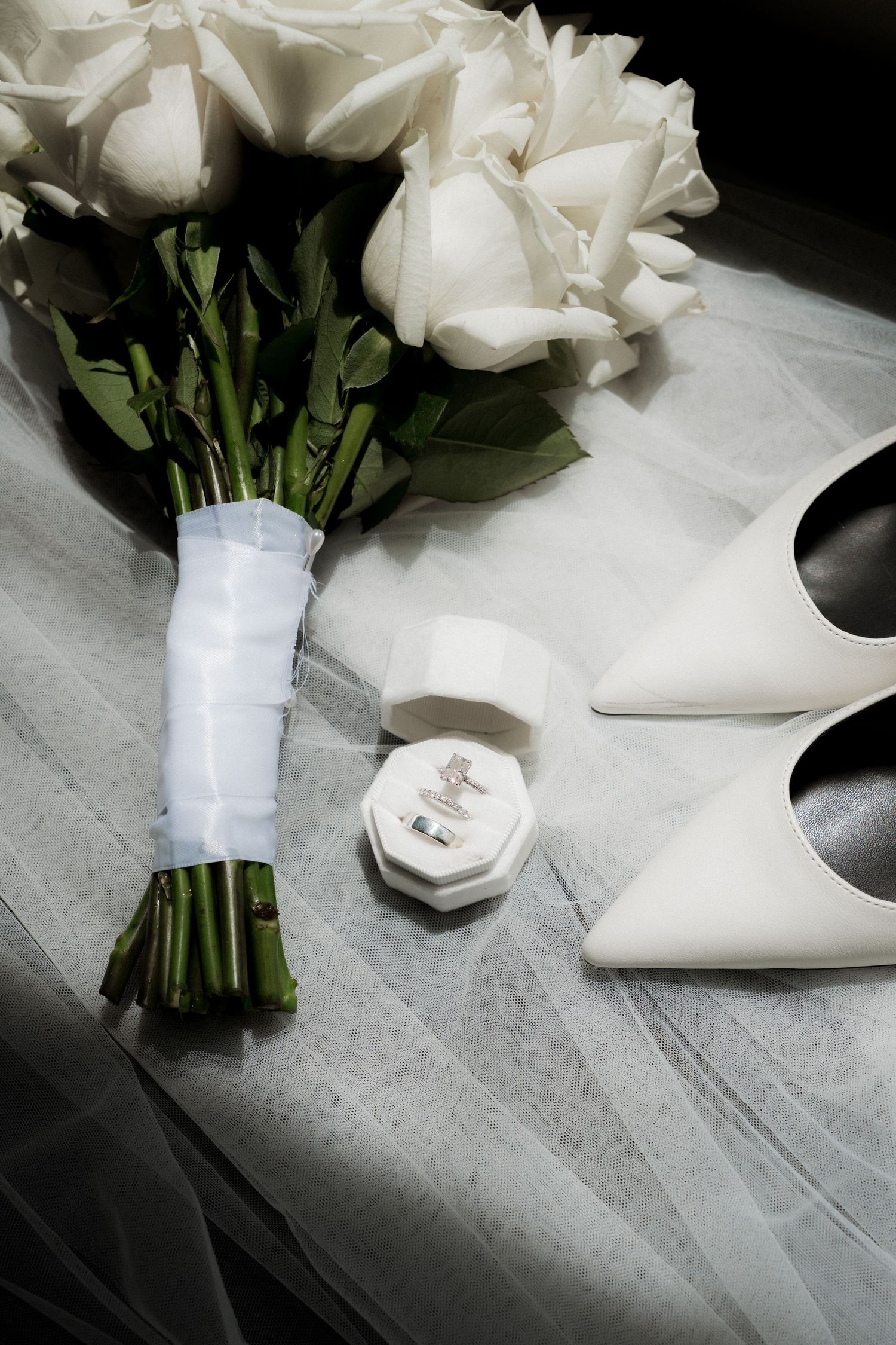 White bridal bouquet and elegant wedding shoes arranged on a light surface.