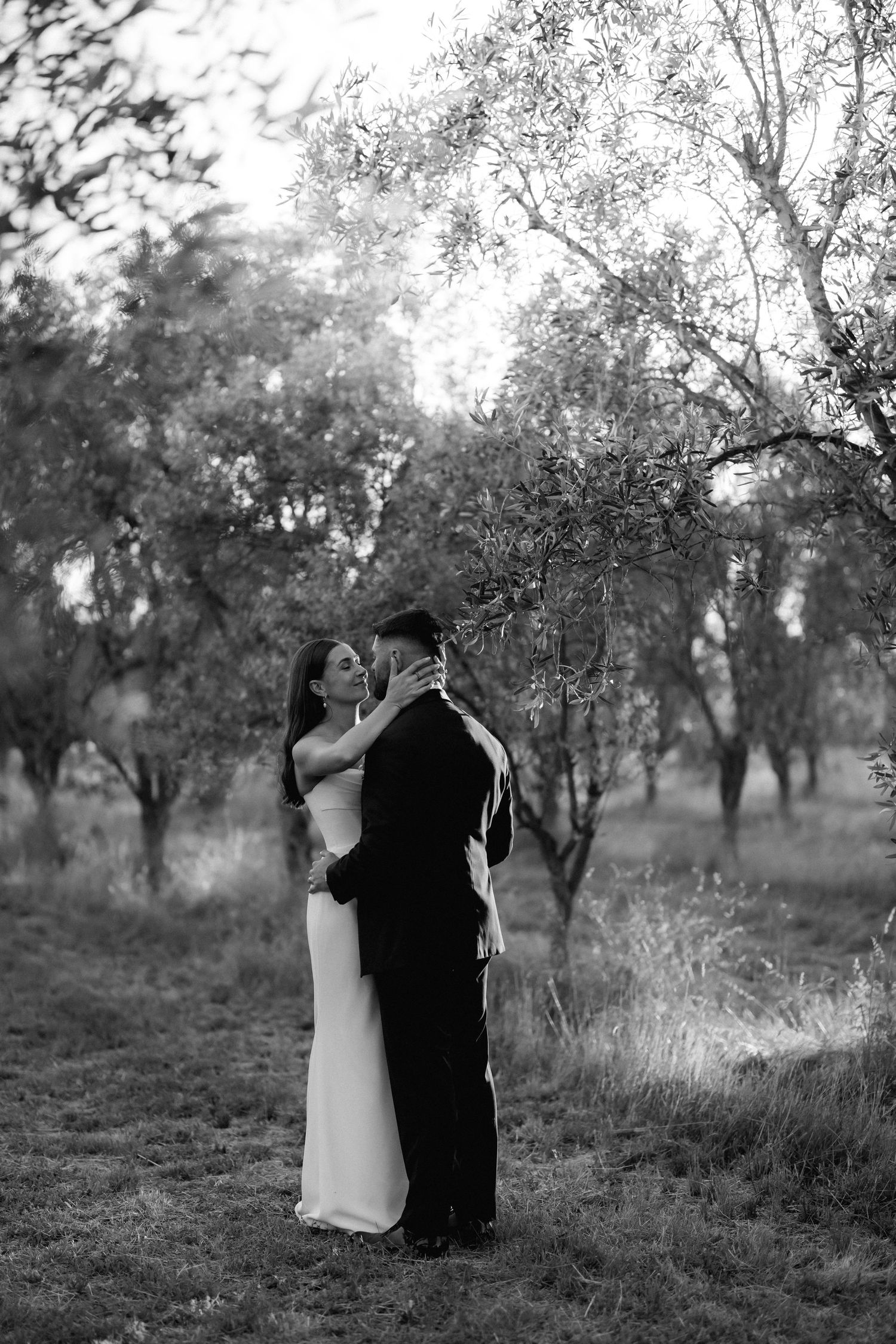 A romantic black and white series of wedding photos captured in a serene outdoor setting with trees.