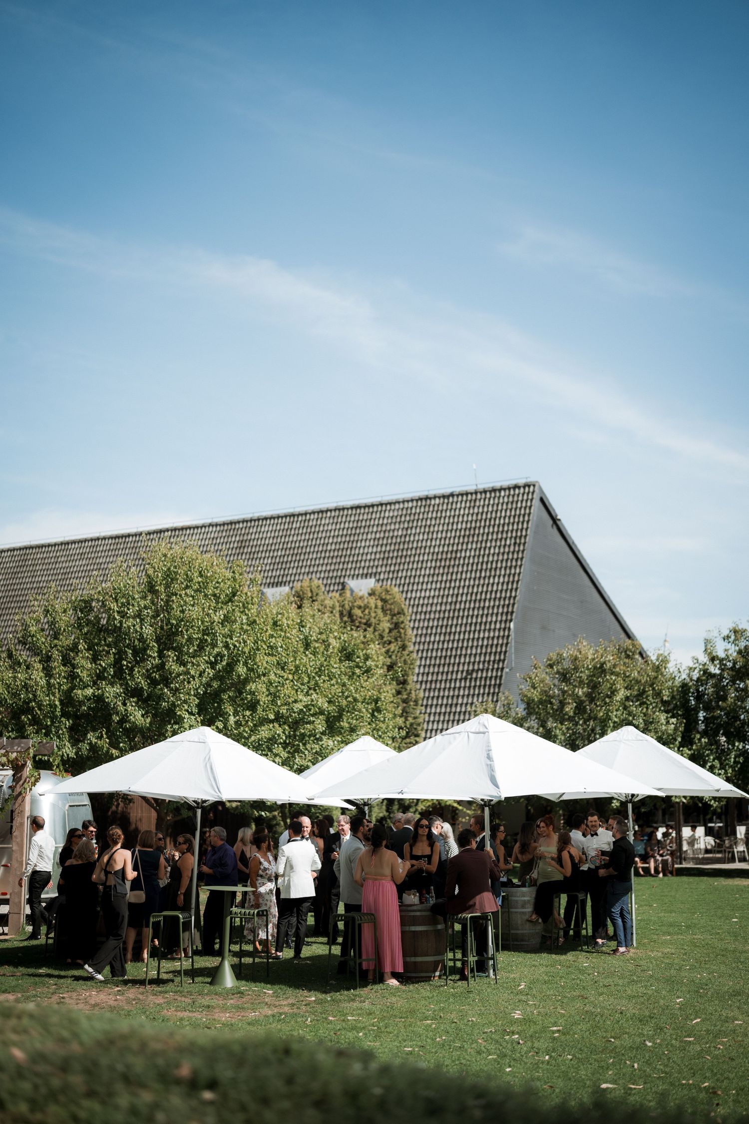Outdoor wedding reception with white tents and guests gathered on a grassy lawn under blue skies.
