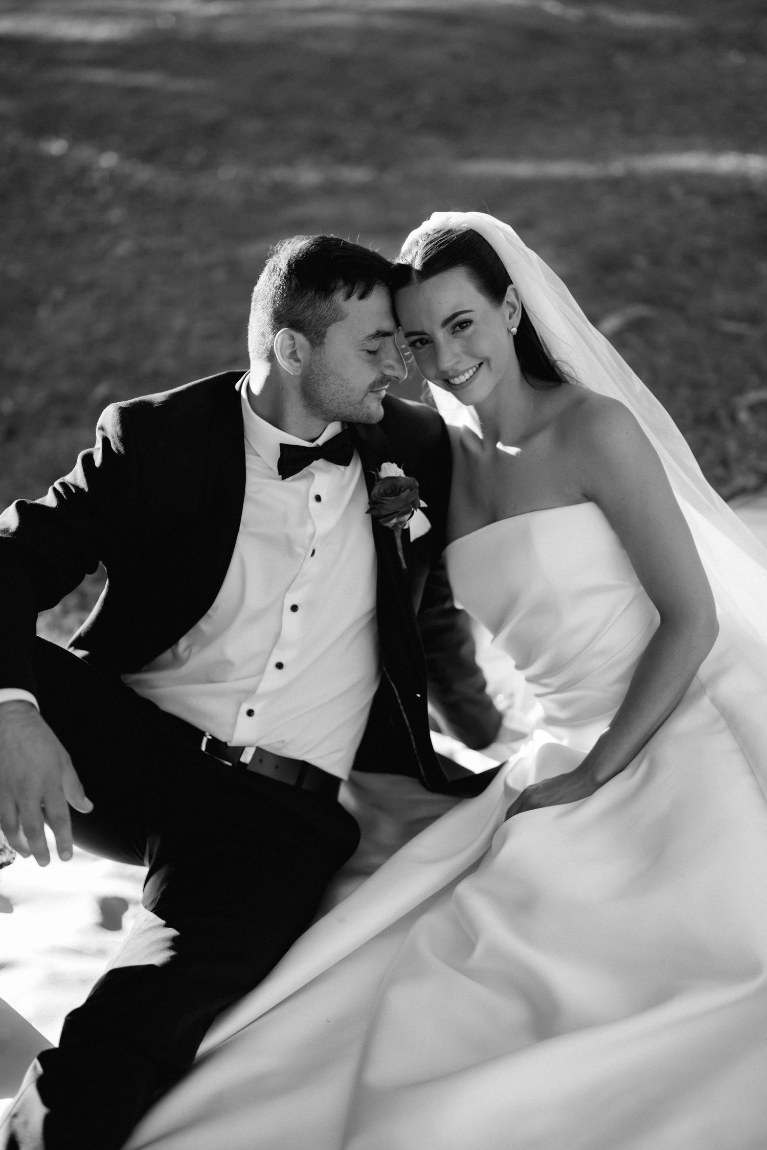 Black and white wedding portrait of a couple in formal attire sharing an intimate moment outdoors.