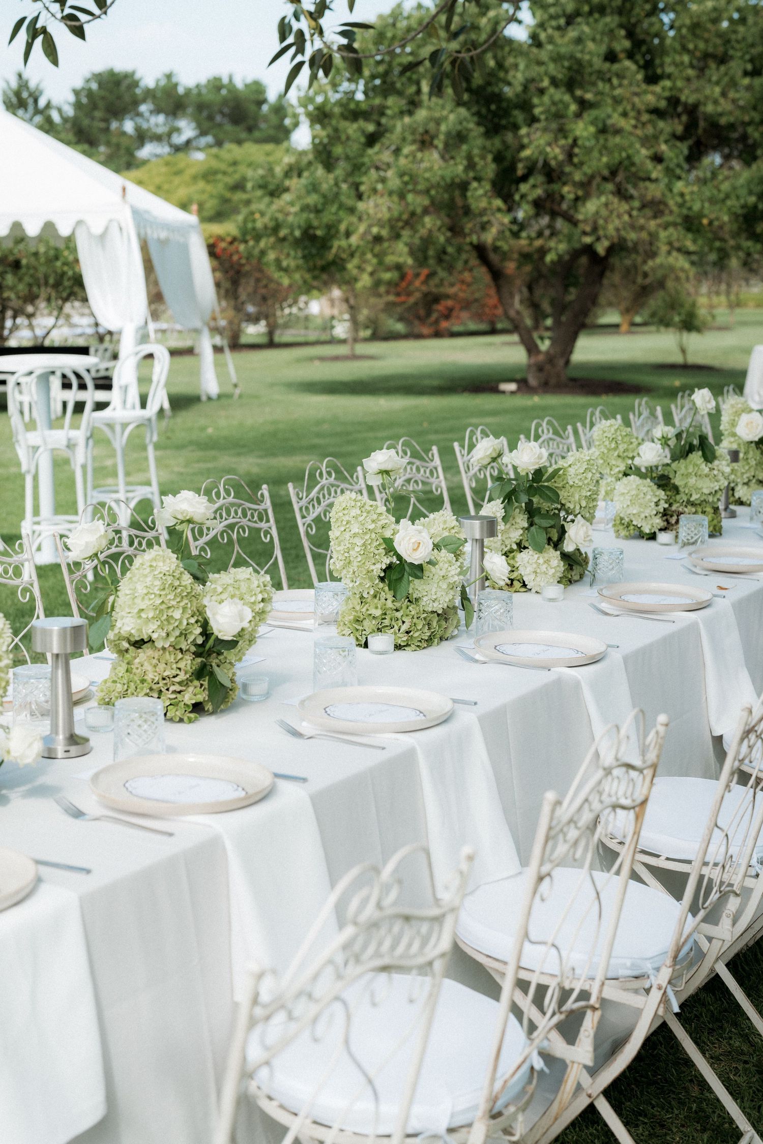 Elegant outdoor wedding reception table set with white linens and floral centerpieces.