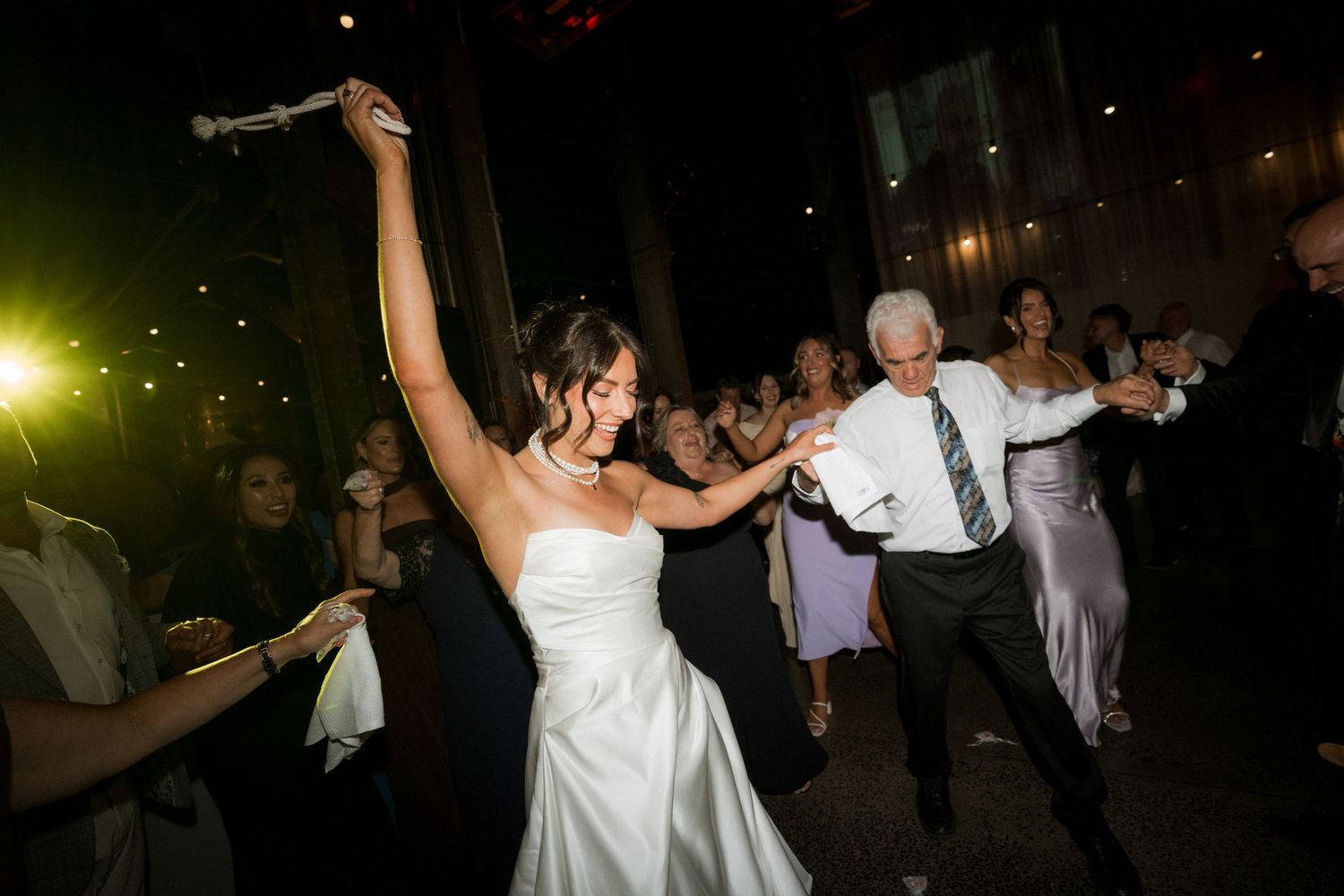 Wedding guests dancing and celebrating on a dark dance floor with festive lighting.