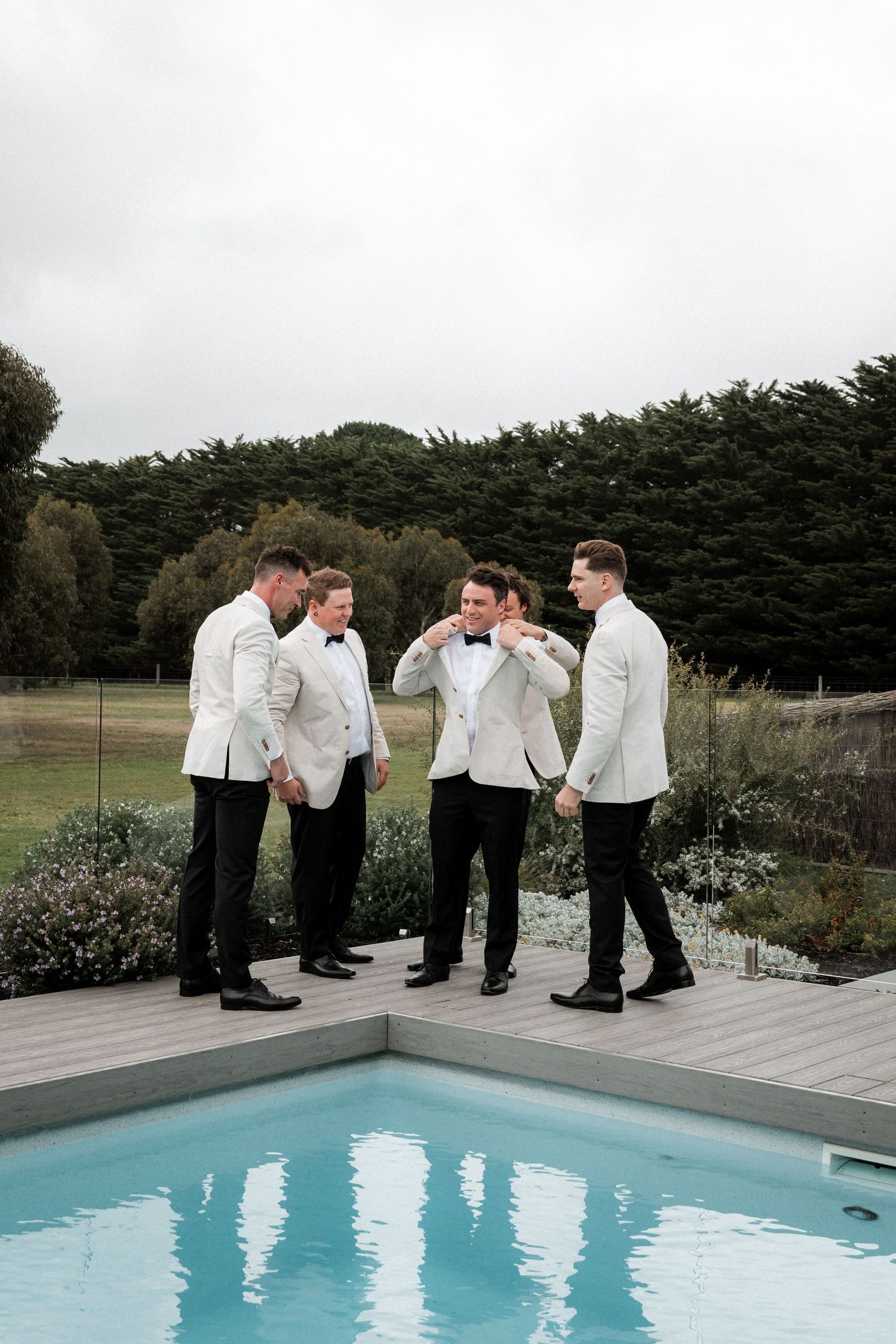 A group in white dress shirts and black pants gather playfully around a swimming pool on an overcast day.