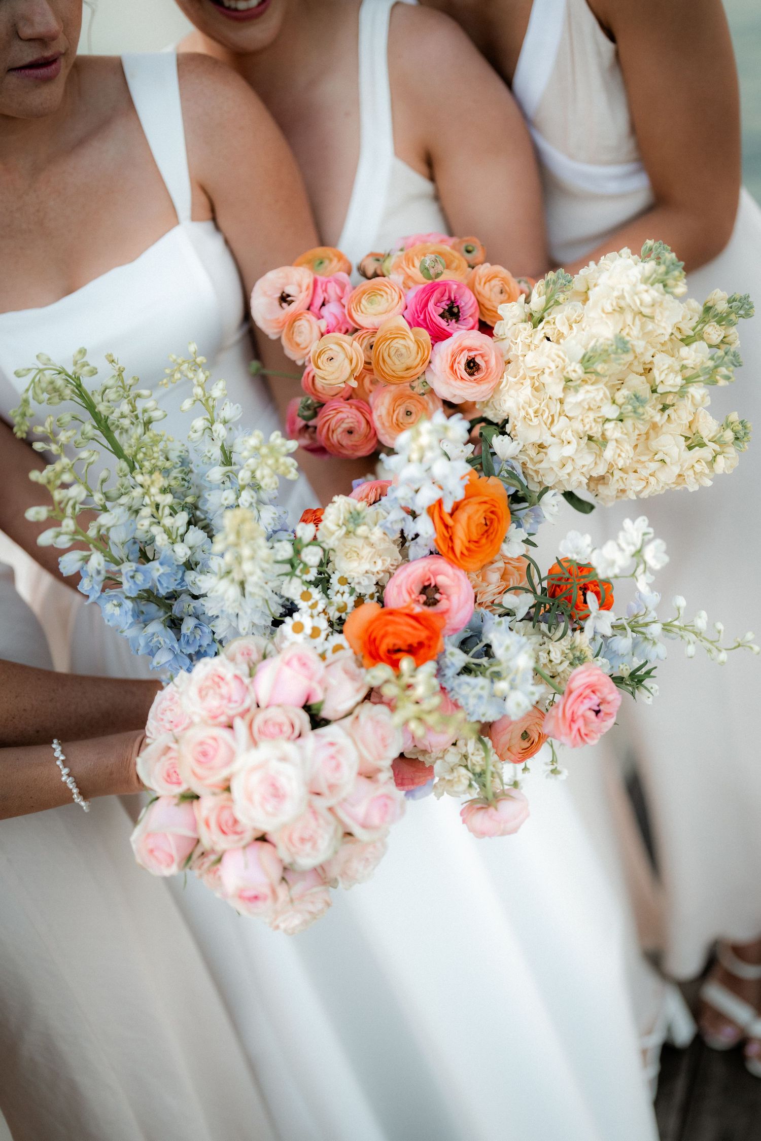 Colorful wedding bouquets featuring pink, orange, and white flowers held in a row.