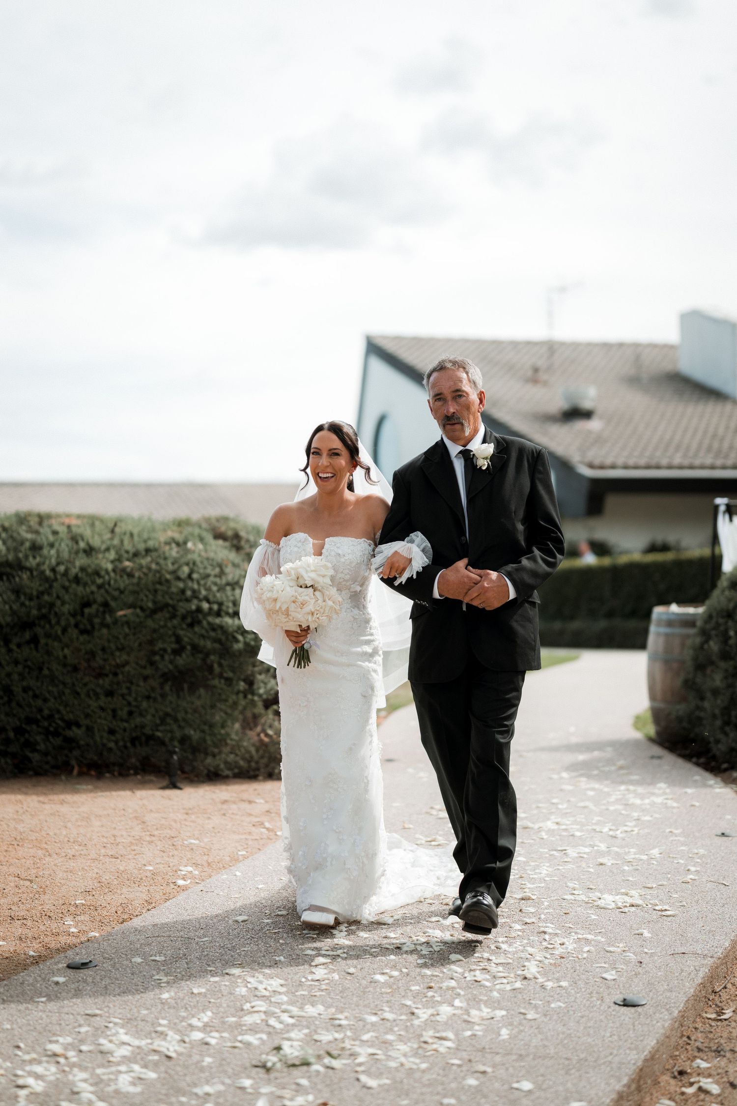 Wedding couple walking along a stone pathway with scattered petals.