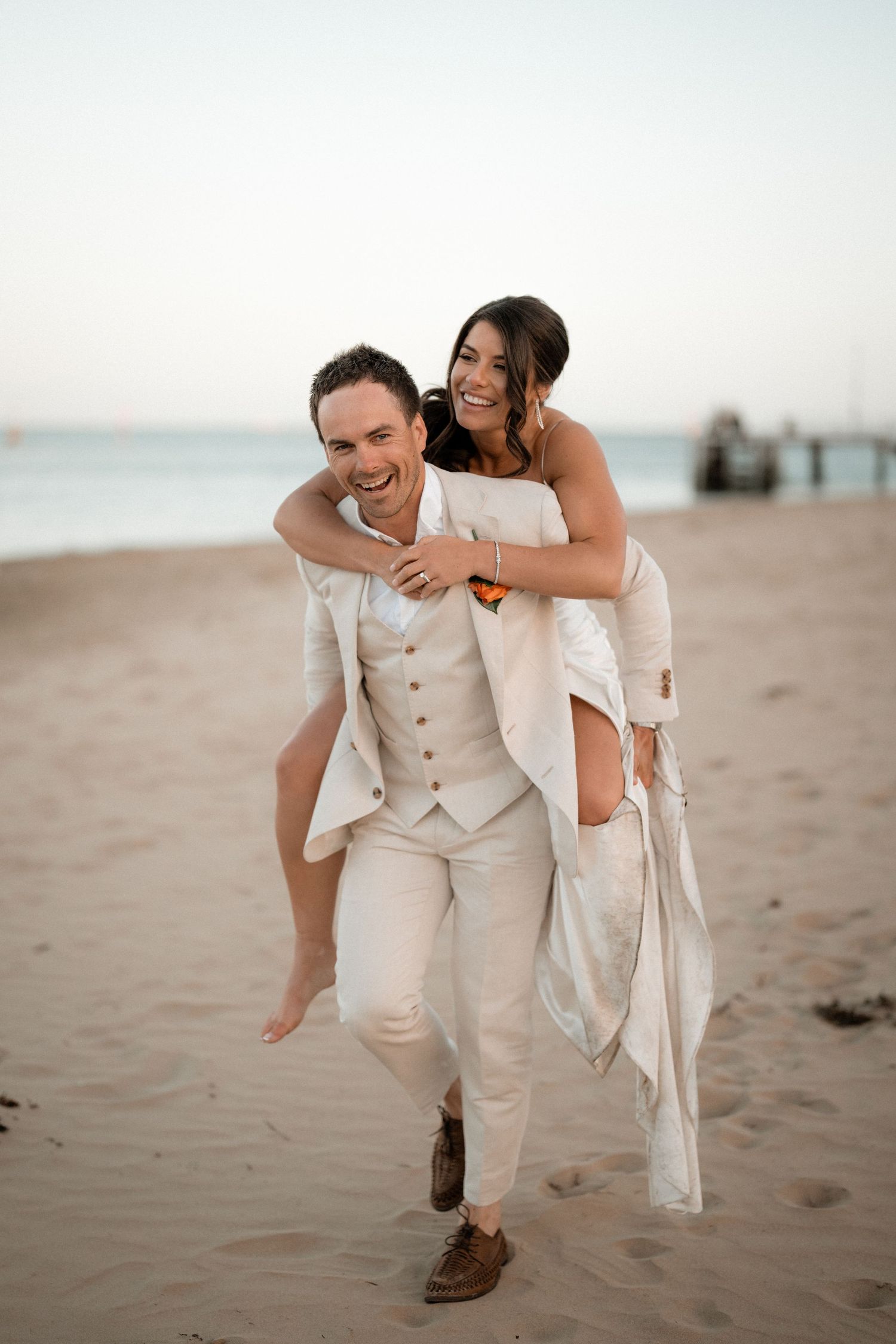A joyful couple shares a playful moment on a sandy beach at sunset.