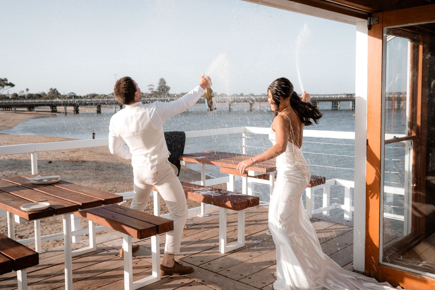 Wedding party in white dresses posing along a wooden dock by the ocean.