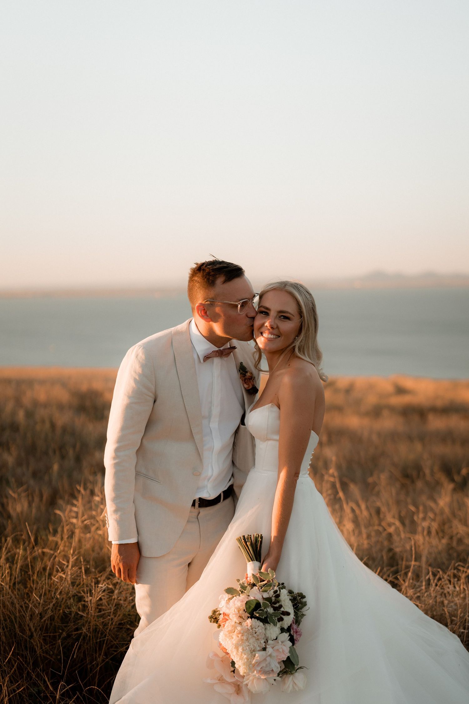 Romantic sunset wedding portrait in a golden field overlooking the ocean.