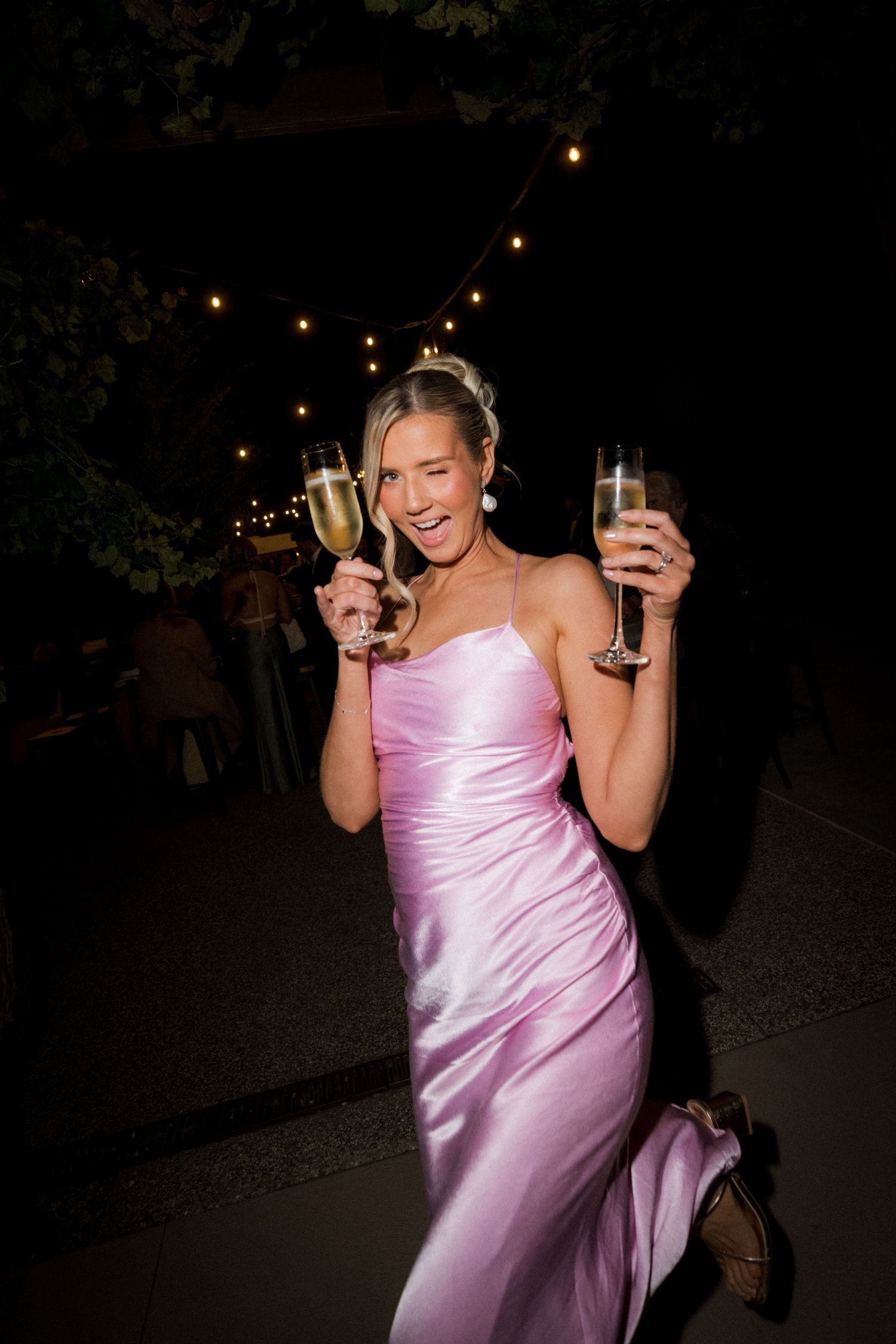 Wedding celebration at night with guests enjoying drinks under string lights.