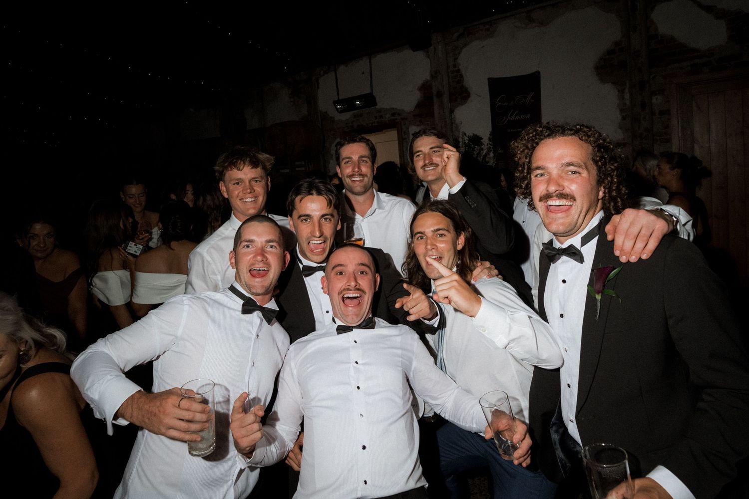 Wedding party in formal attire celebrating and posing together in a dark indoor setting.