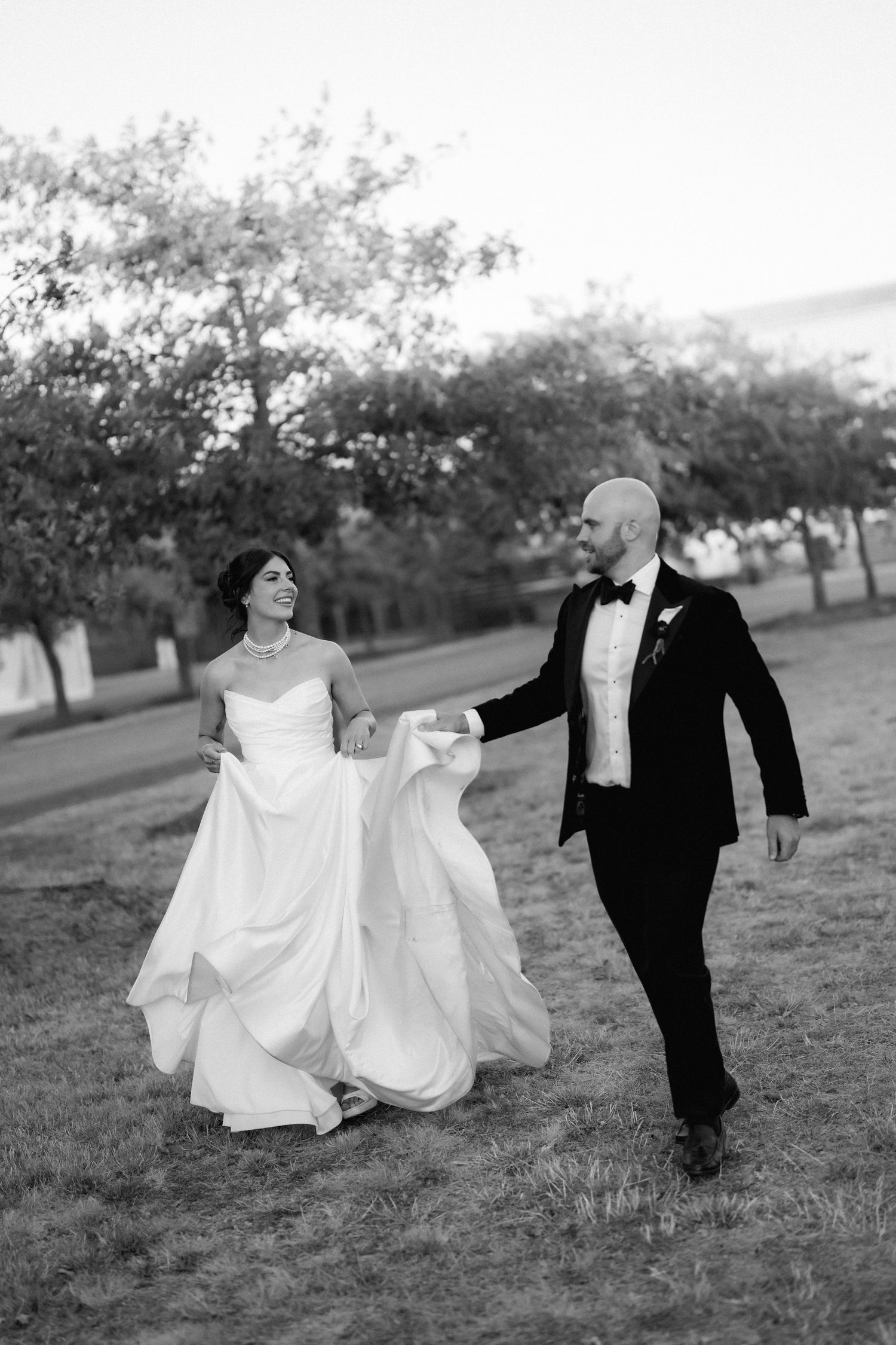 Black and white wedding photos of a couple running playfully through an orchard.