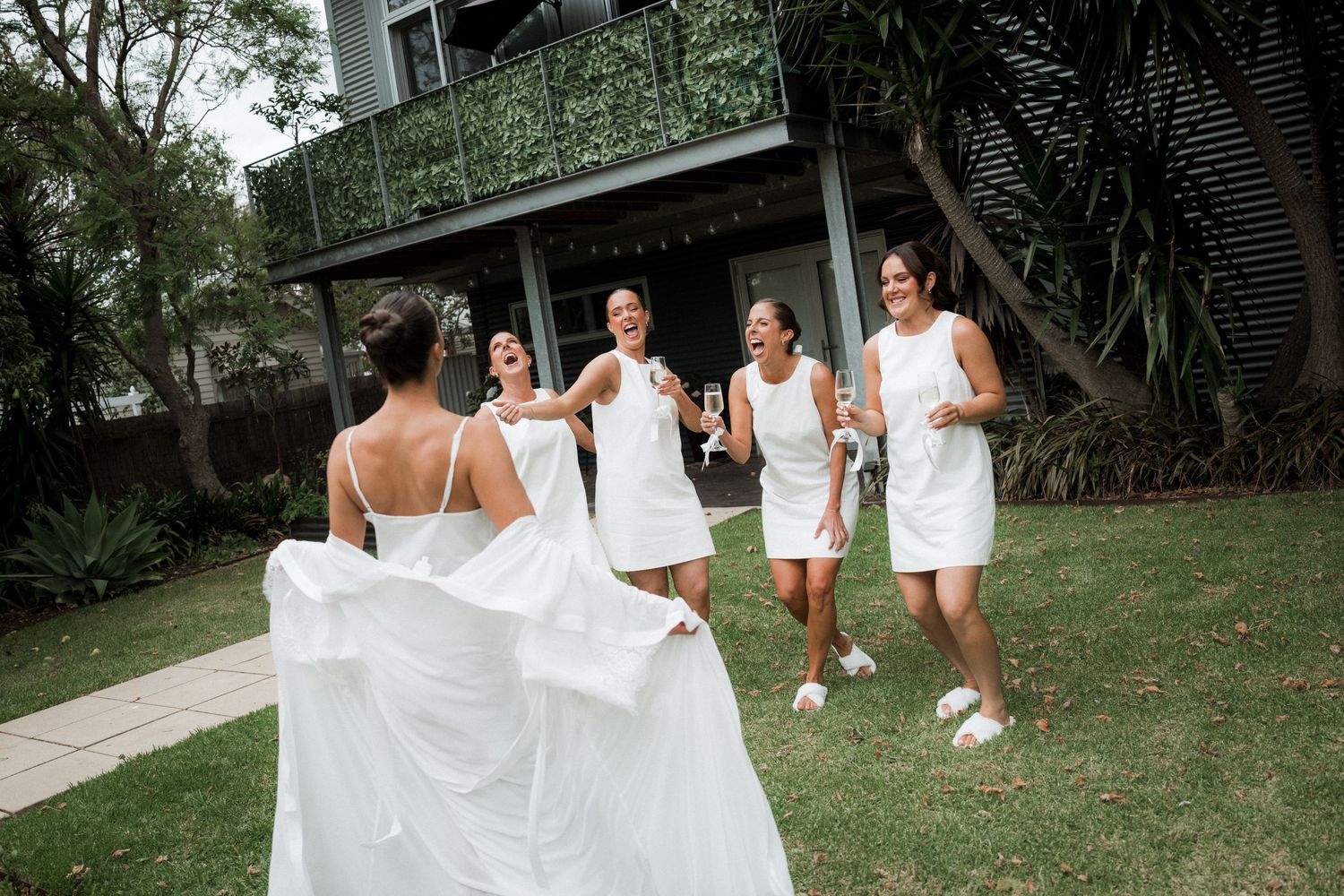 Bride in white gown with bridesmaids in white dresses celebrating outdoors at a wedding.