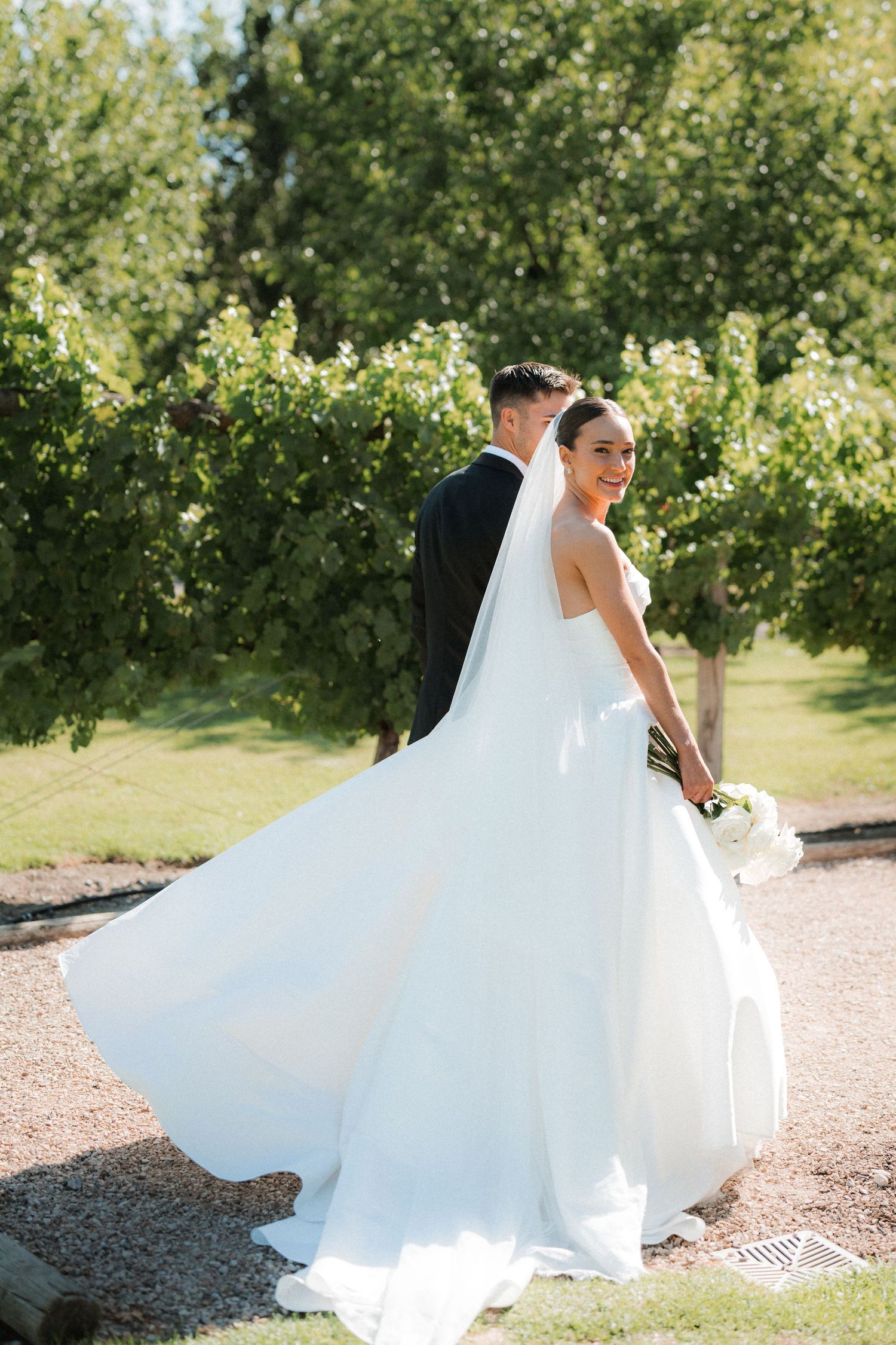 A flowing white wedding dress billows in the breeze against a sunny garden backdrop.