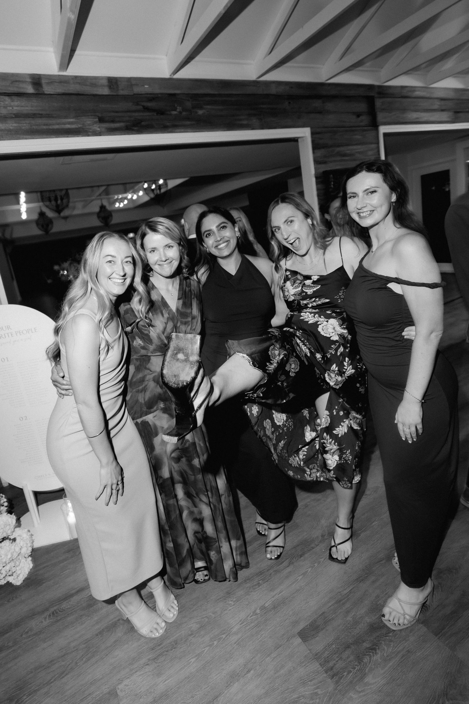 Group of wedding guests dancing and posing on a wooden dance floor at reception.