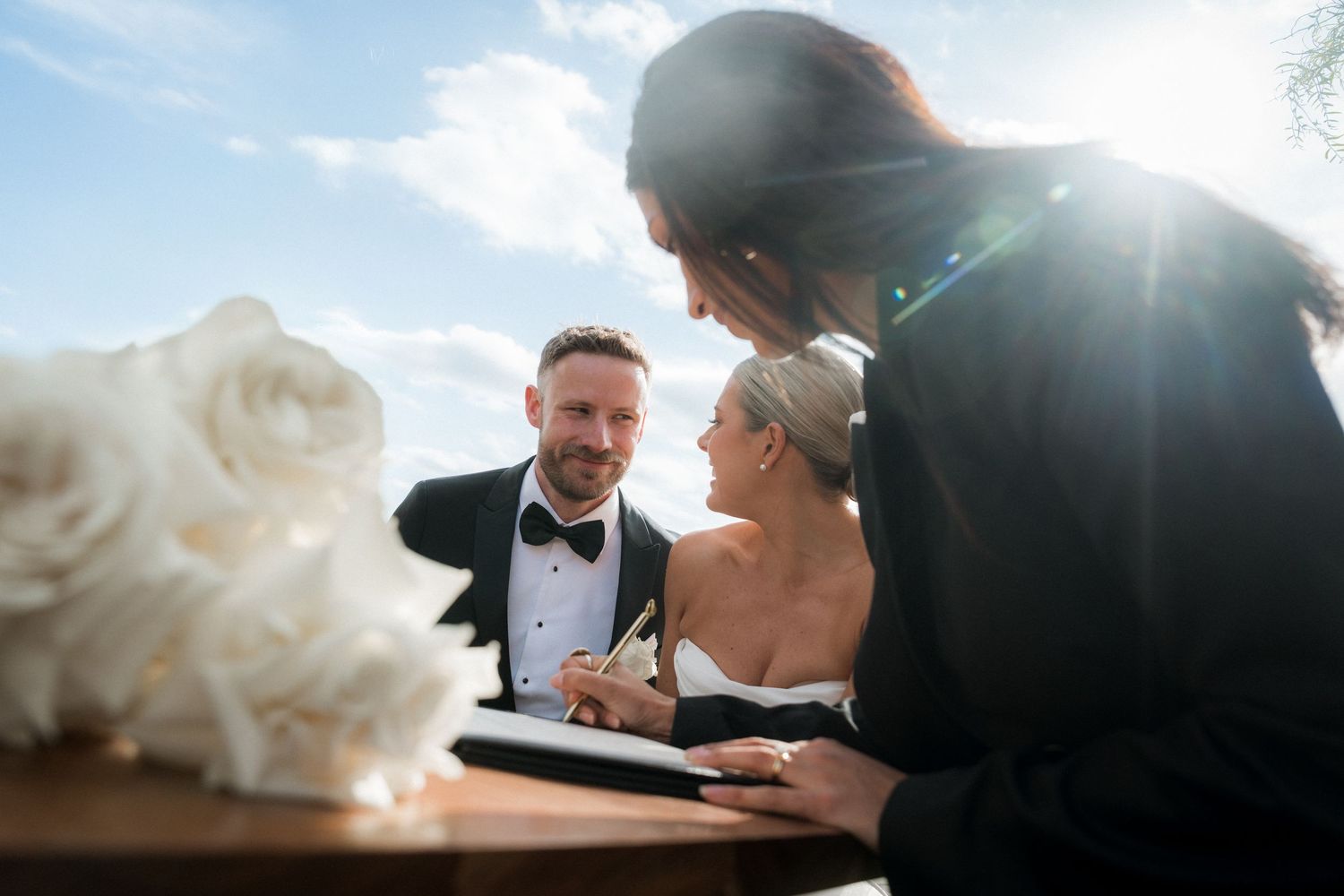 Romantic wedding couple embraces in soft sunlight creating silhouettes against a dreamy sky background.