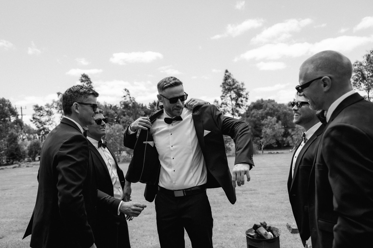 A black and white panoramic sequence shows a celebratory group dancing together outdoors at a festive gathering.