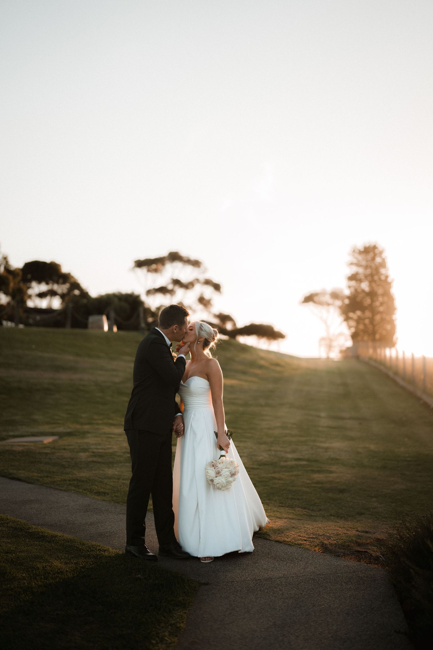 Romantic sunset wedding portrait of couple embracing on hillside path.