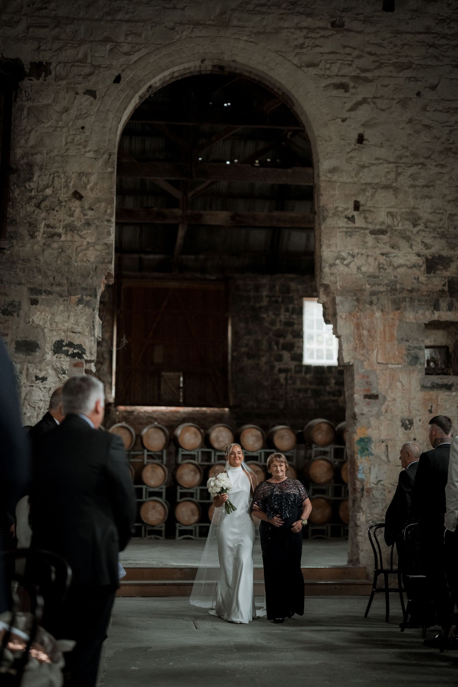 A wedding ceremony in a rustic wine cellar with stone walls and wooden barrels creating an atmospheric backdrop.