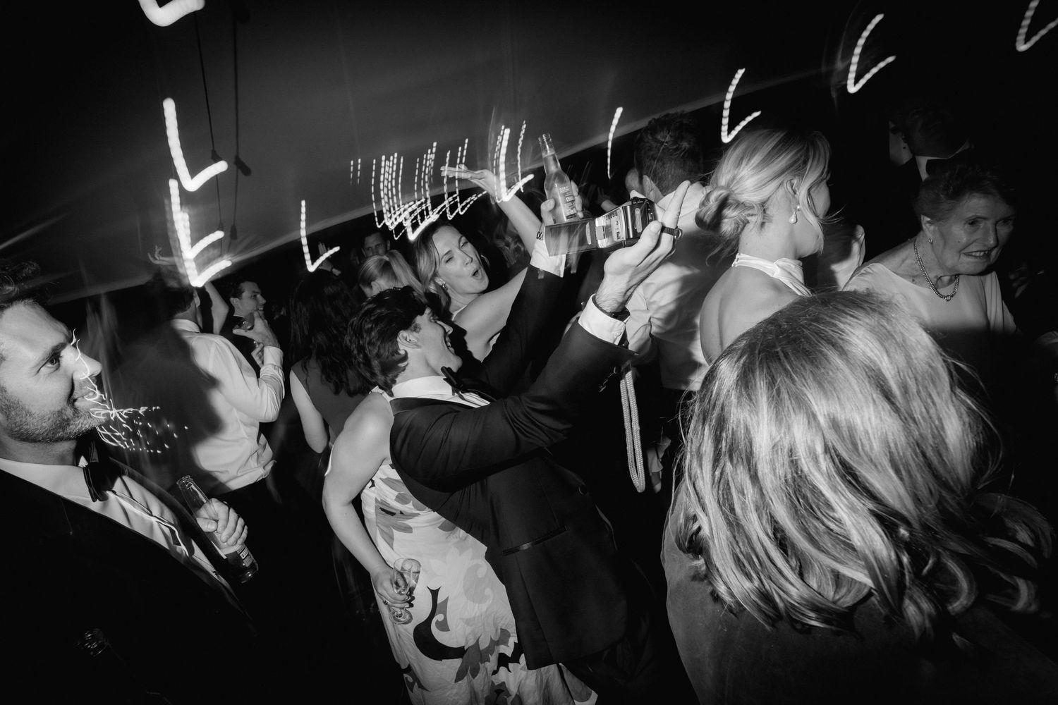 Black and white photo of energetic dancing and celebrating at a nighttime wedding reception.