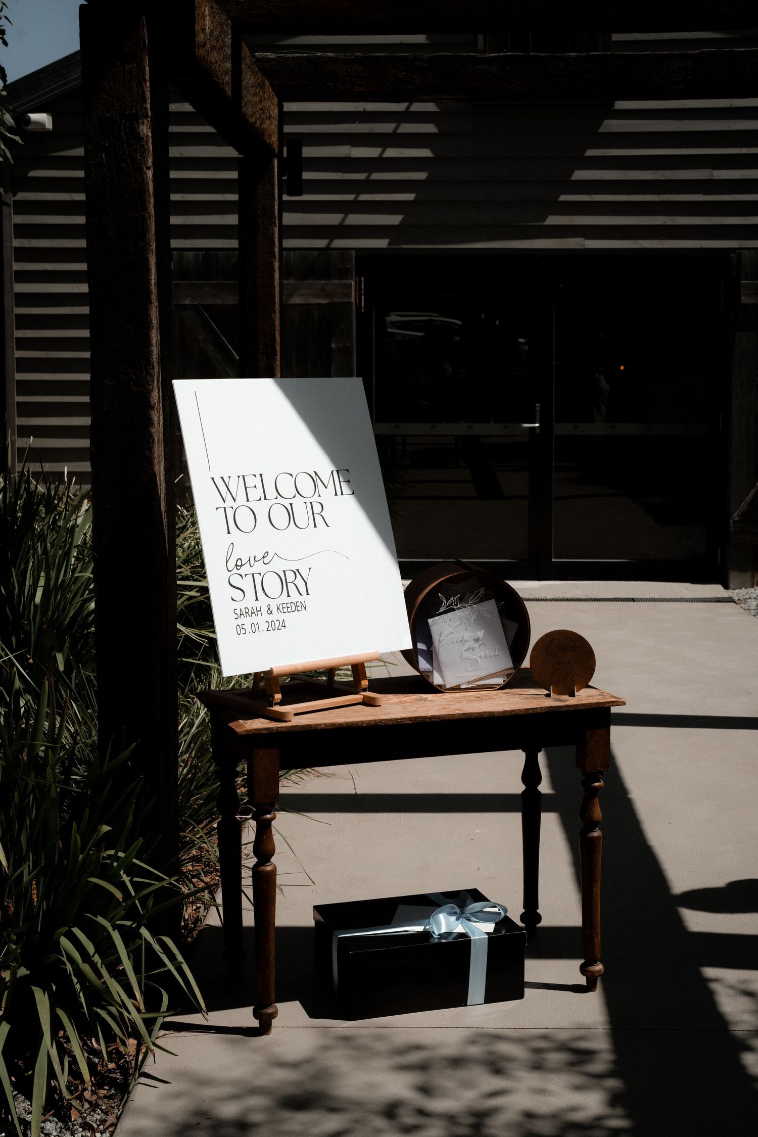 Welcome sign displayed on rustic wooden table with shadows casting on a sunlit entrance.
