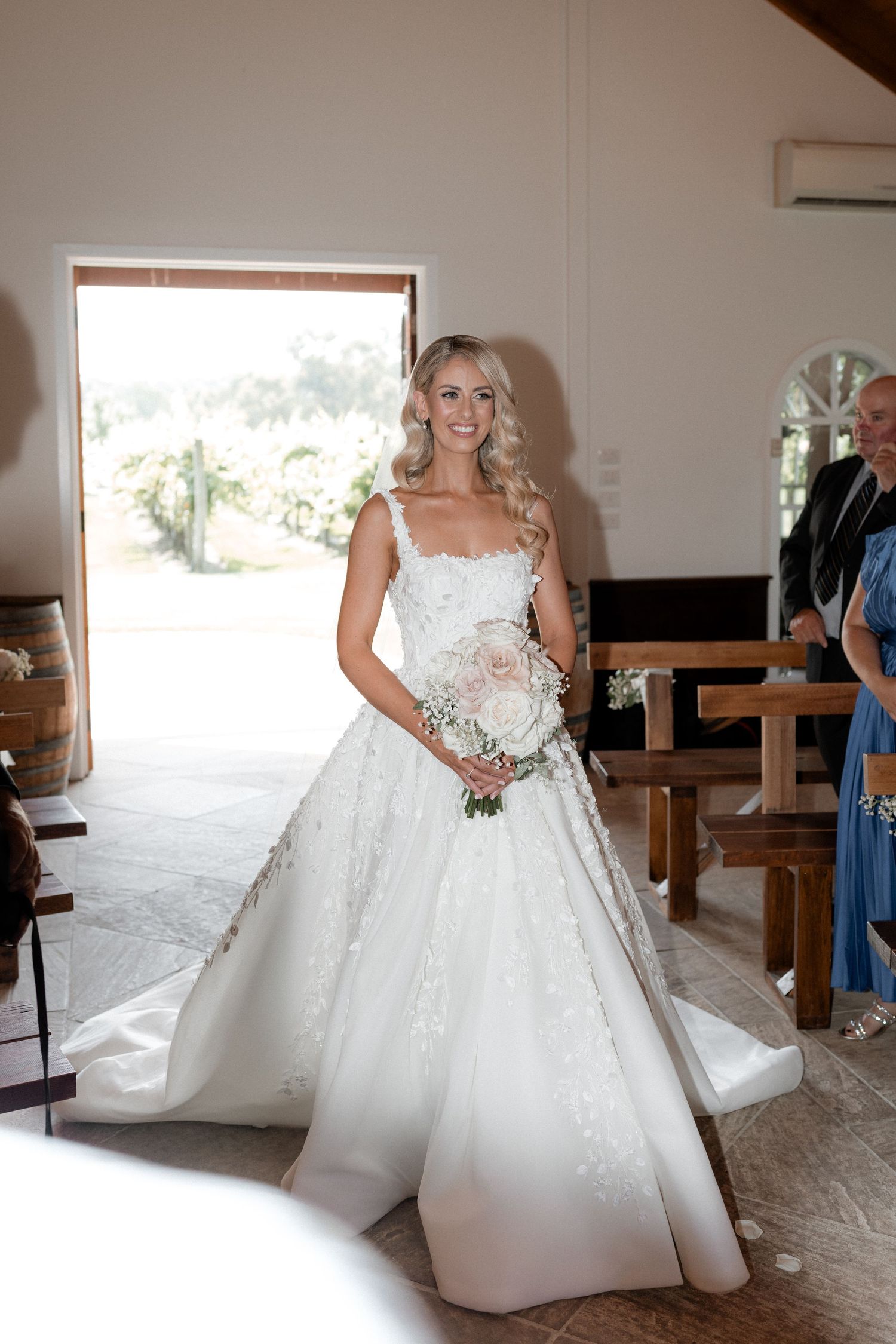Elegant bride in a white lace ball gown poses in front of a bright window.