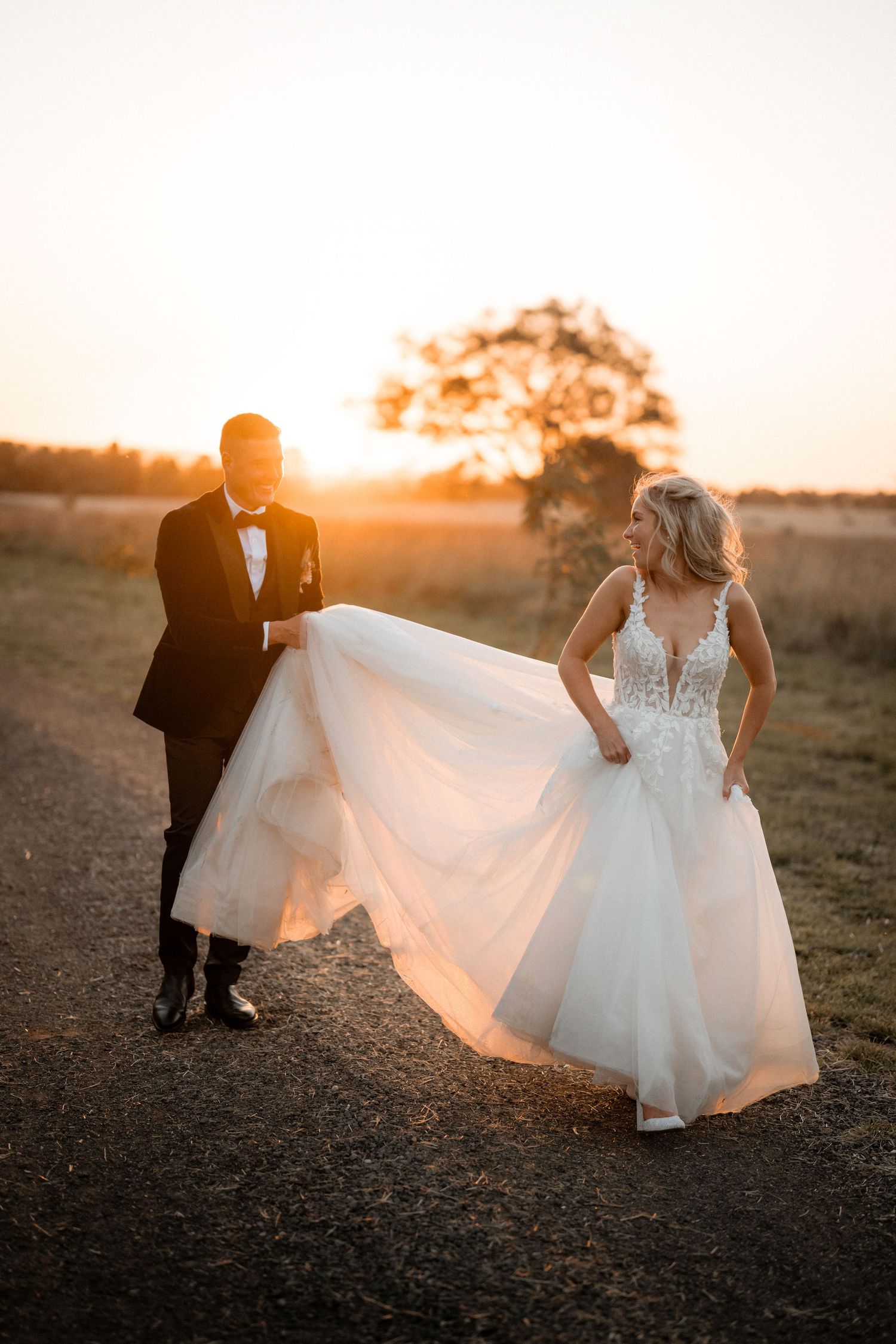 Dreamy golden hour wedding portrait with couple walking as bride's dress flows in evening light.