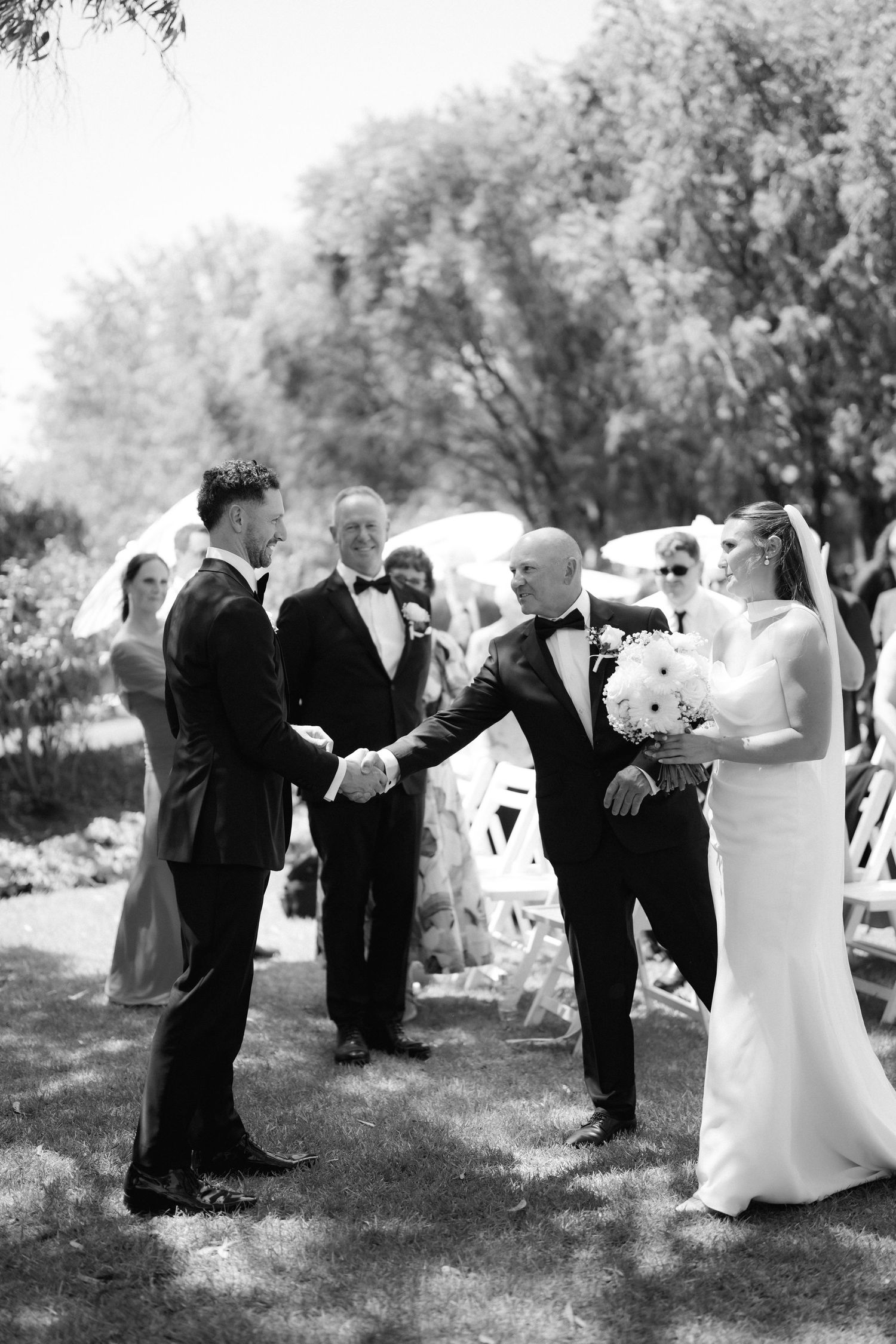 A wedding party performs a synchronized dance move in a black and white photo outdoors.