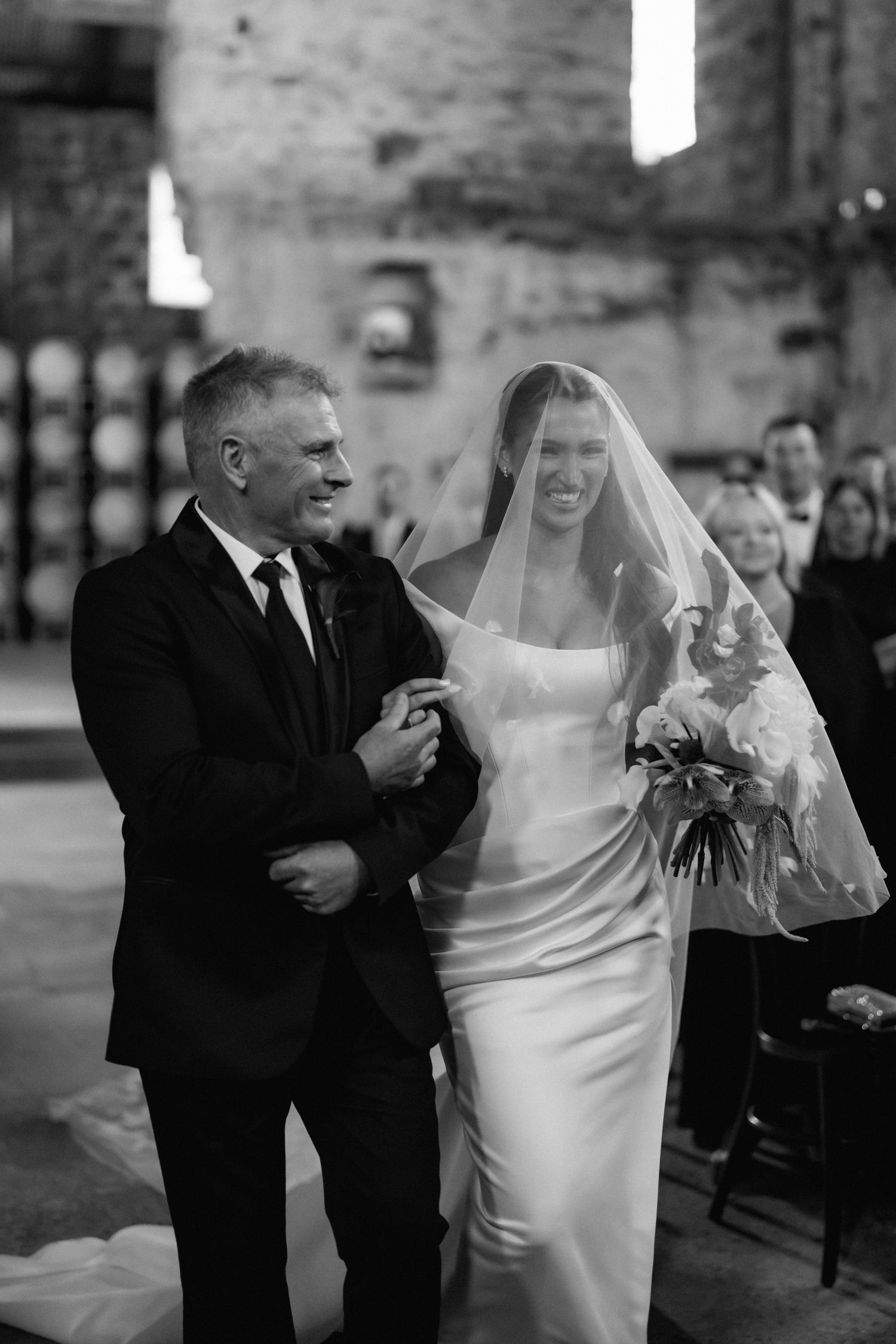 A tender moment during a traditional wedding ceremony in a stone-walled venue with the bride in an elegant white gown.