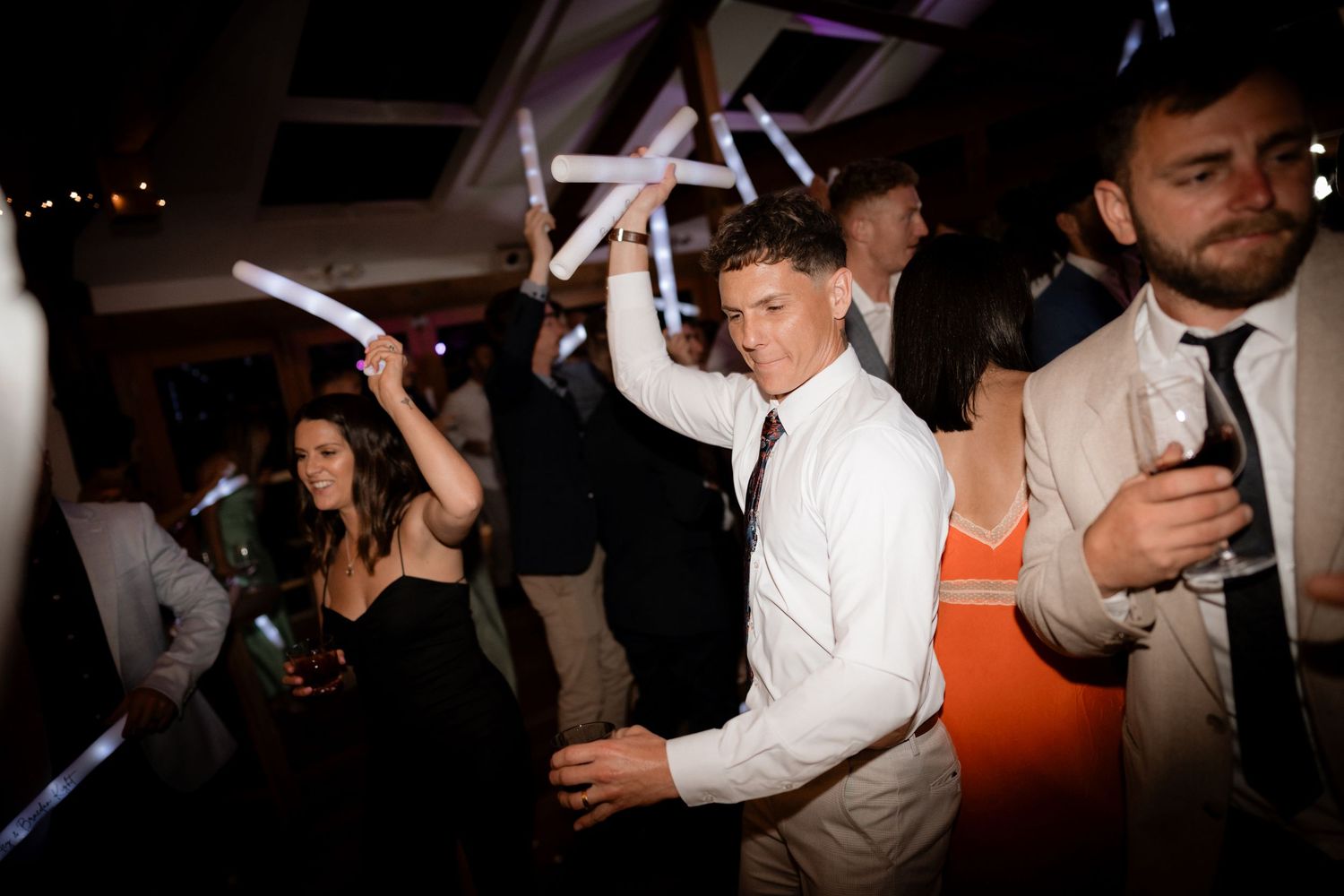 Wedding reception dance floor moments captured in dramatic lighting with guests celebrating.