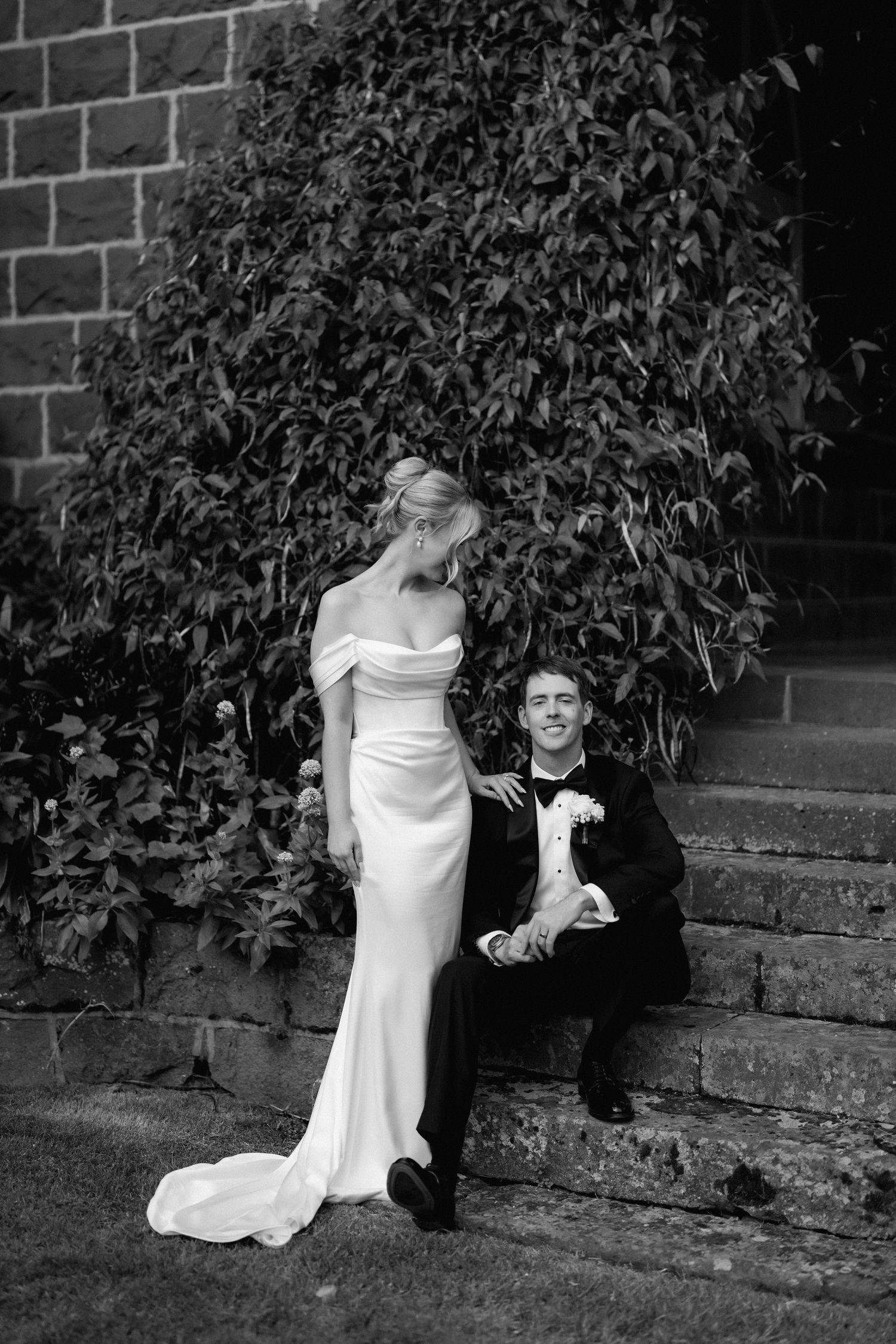Black and white wedding portraits taken against a brick wall with climbing vines.