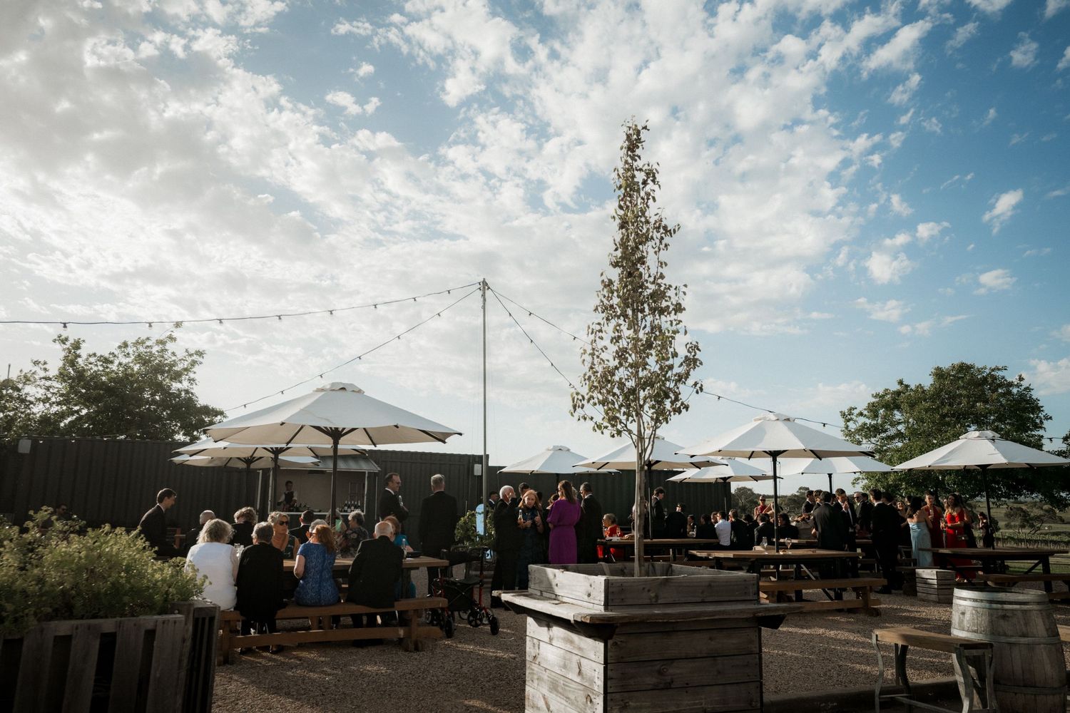 Wedding reception venue setup outdoors with white tents and tables under a bright blue sky.