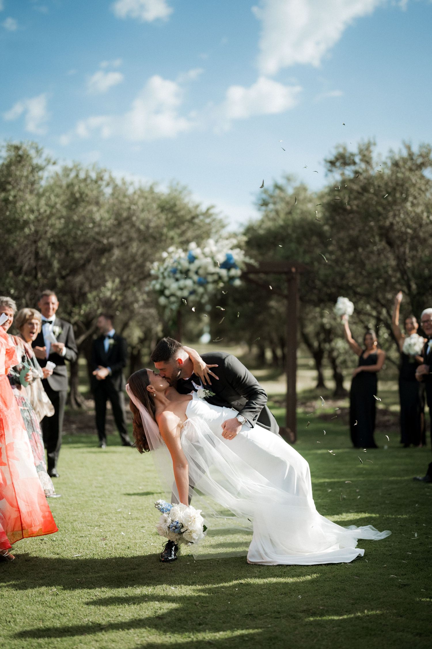 Wedding party members tossing confetti and celebrating on a sunny lawn.