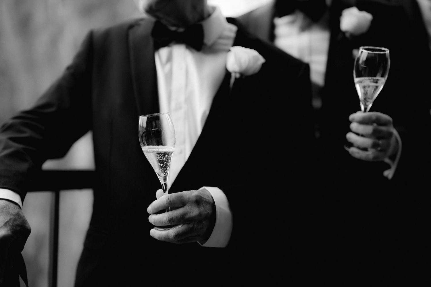 Two people in formal attire hold champagne glasses in black and white photography.