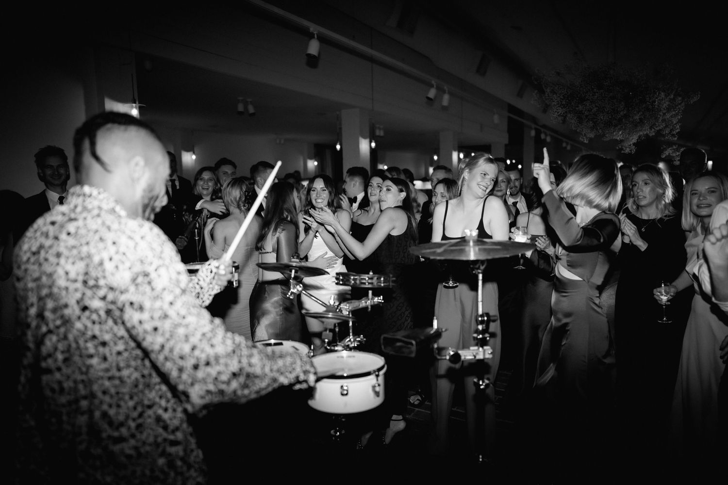 A black and white photo of guests dancing and celebrating at a wedding reception.