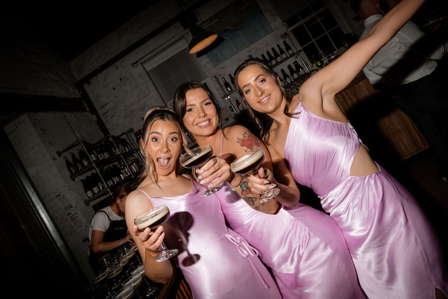 Bridesmaids in pink dresses celebrate joyfully on dance floor during wedding reception.