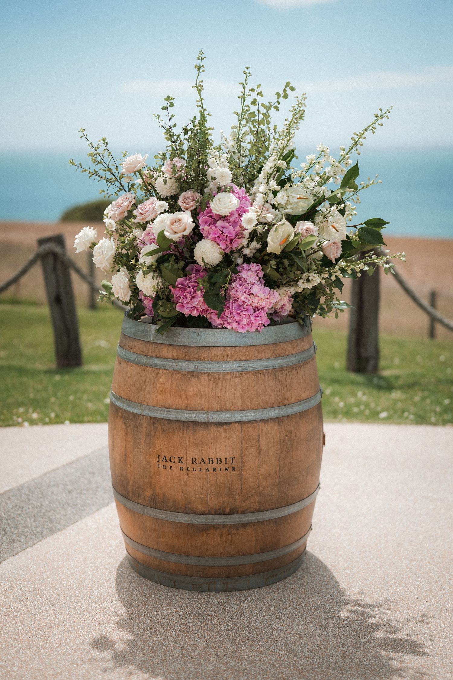 Elegant garden flower arrangement with roses and greenery in a wooden wine barrel by the ocean.