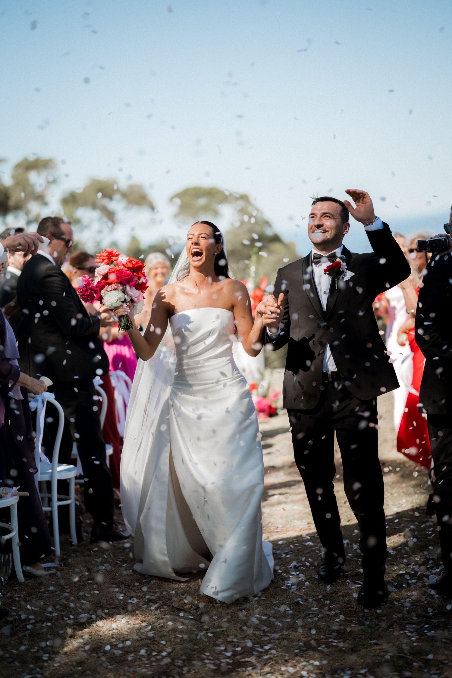Wedding guests toss confetti at the happy couple during an outdoor ceremony celebration.